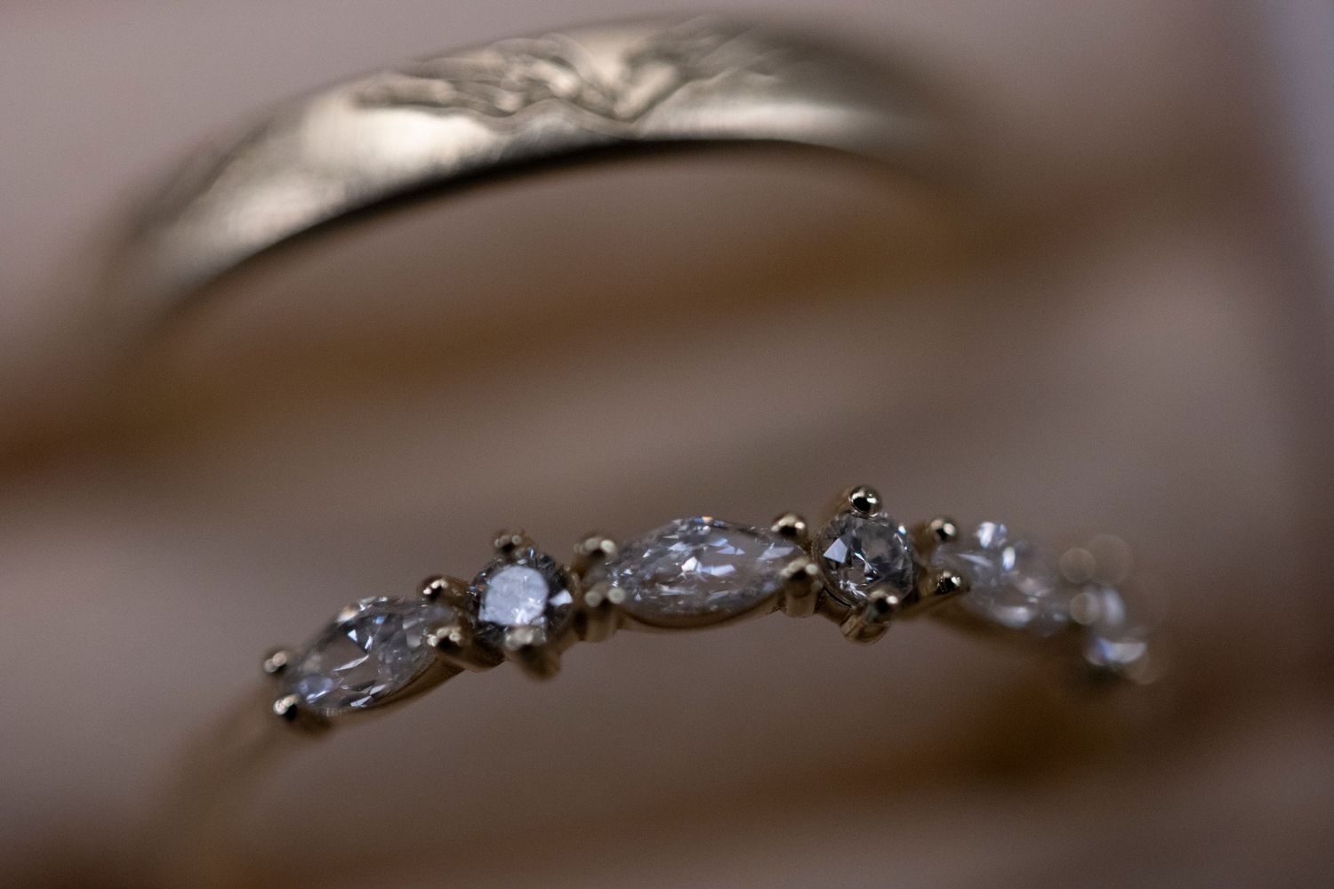 A delicate silver ring with small diamonds arranged in a floral pattern sparkles against a soft brown background.