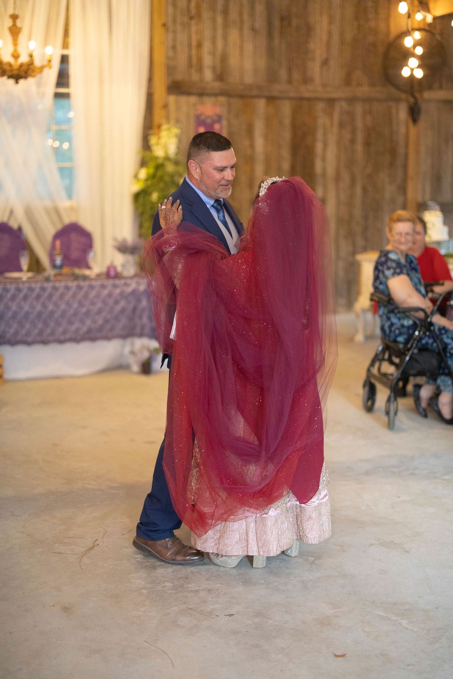 A couple dances in an elegant ballroom setting with chandeliers and ornate decor in the background.