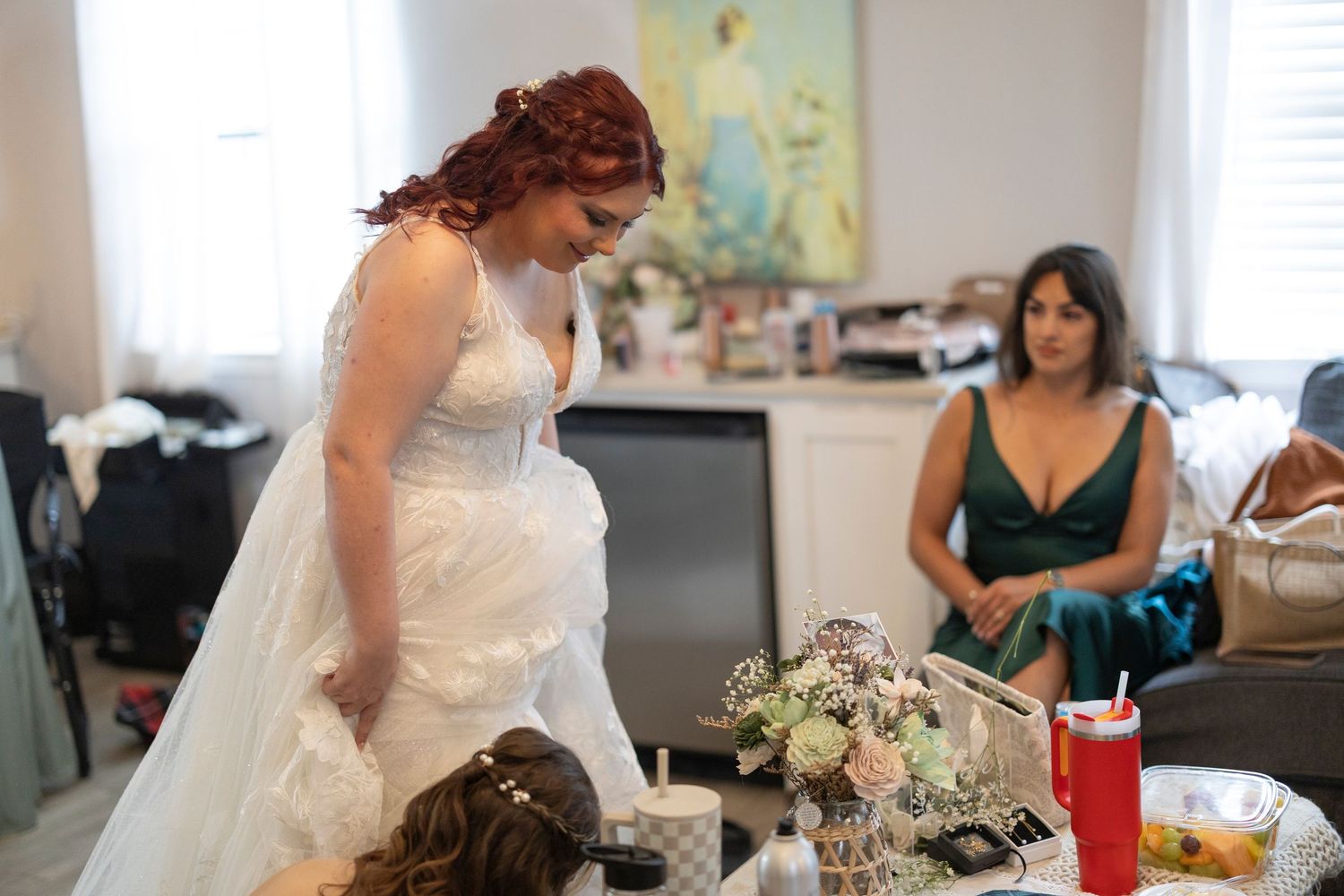 A bride in a white wedding dress prepares for her special day while surrounded by loved ones.