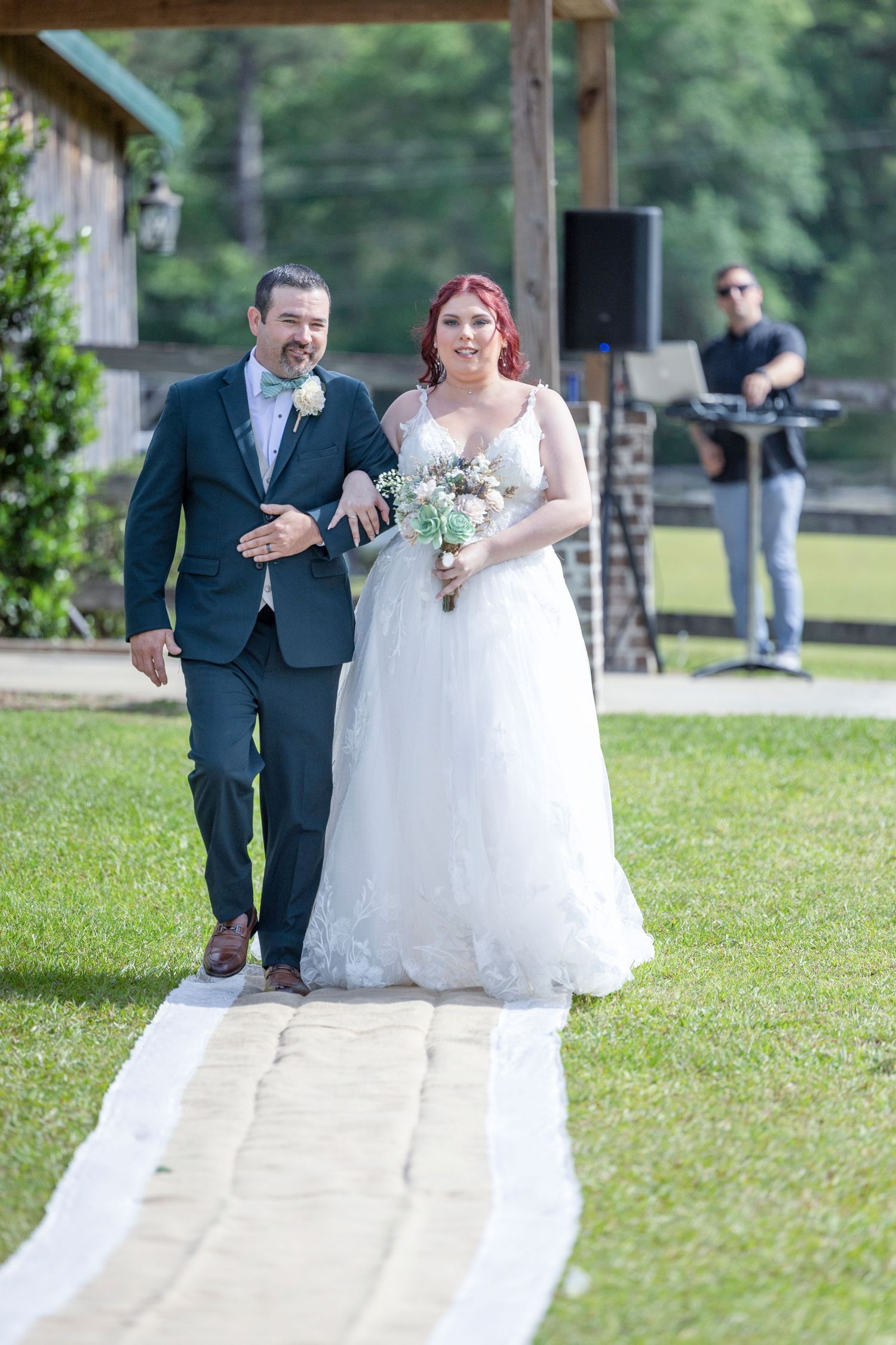 A bride and groom walk down an outdoor aisle lined with white fabric at a garden wedding ceremony.