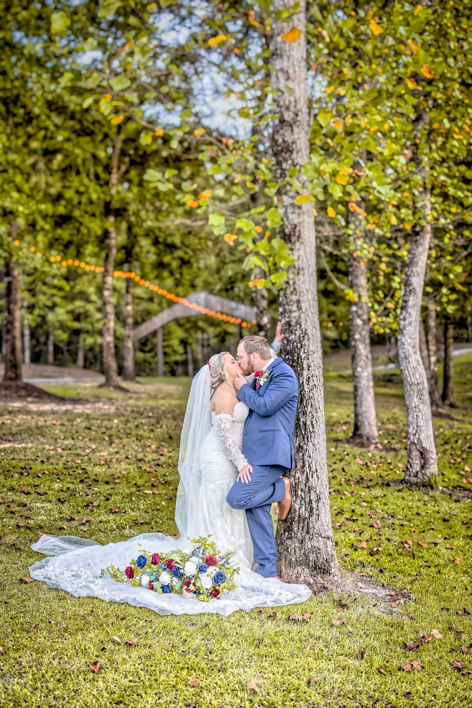 A romantic wedding couple shares intimate moments in a sunlit wooded area with scattered fall leaves on the ground.