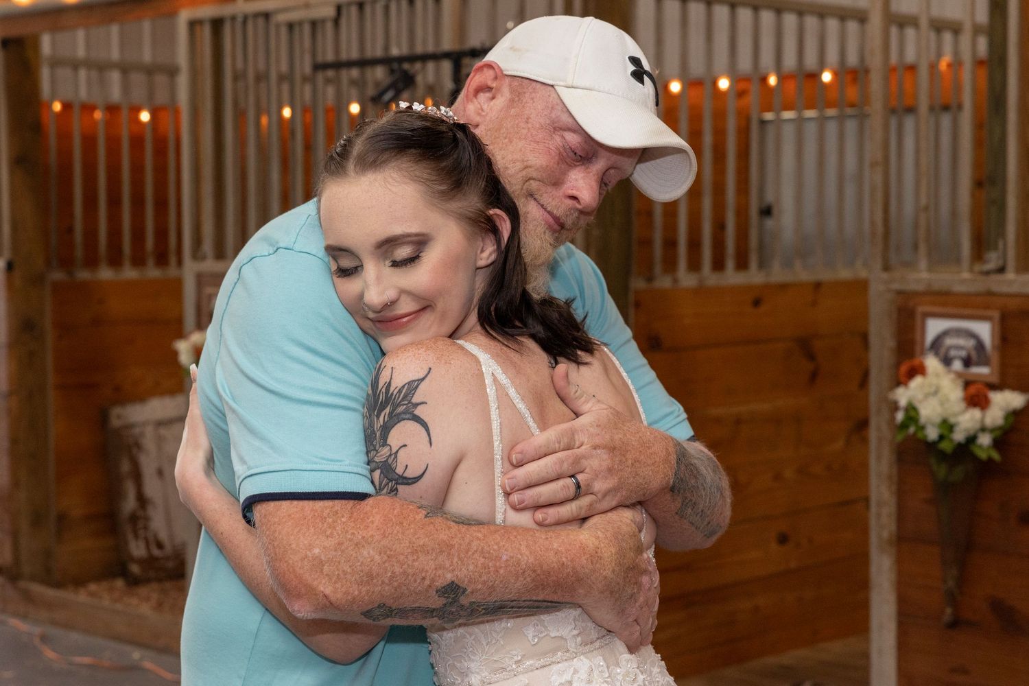 A warm emotional moment captured at a rustic barn wedding venue with string lights in the background.
