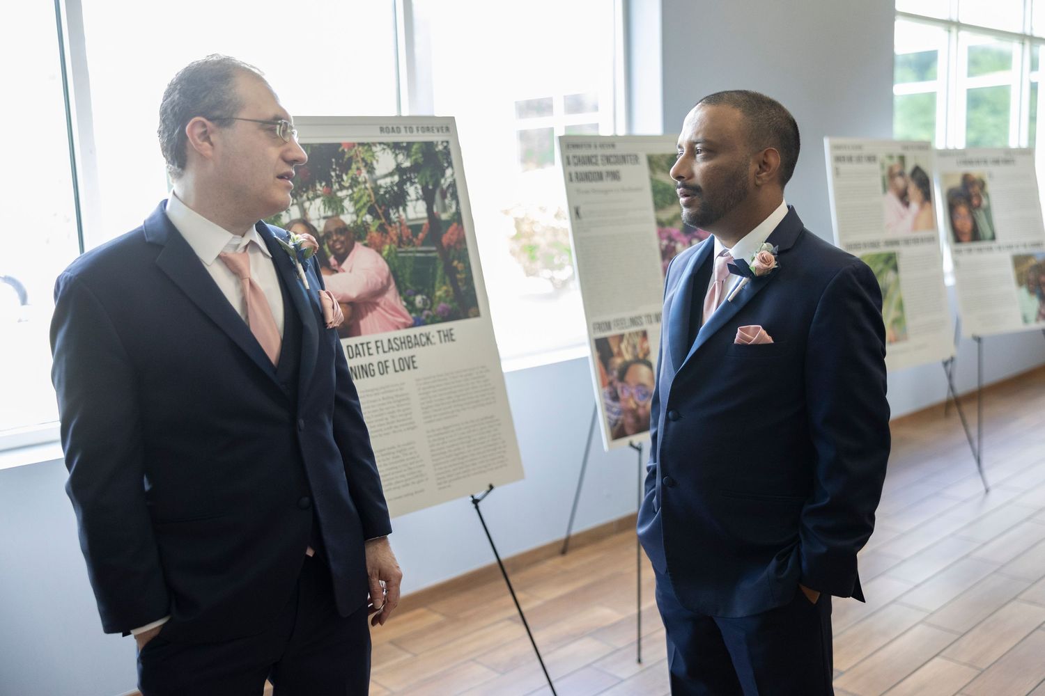 Two men in suits conversing at a formal event with display boards in the background.