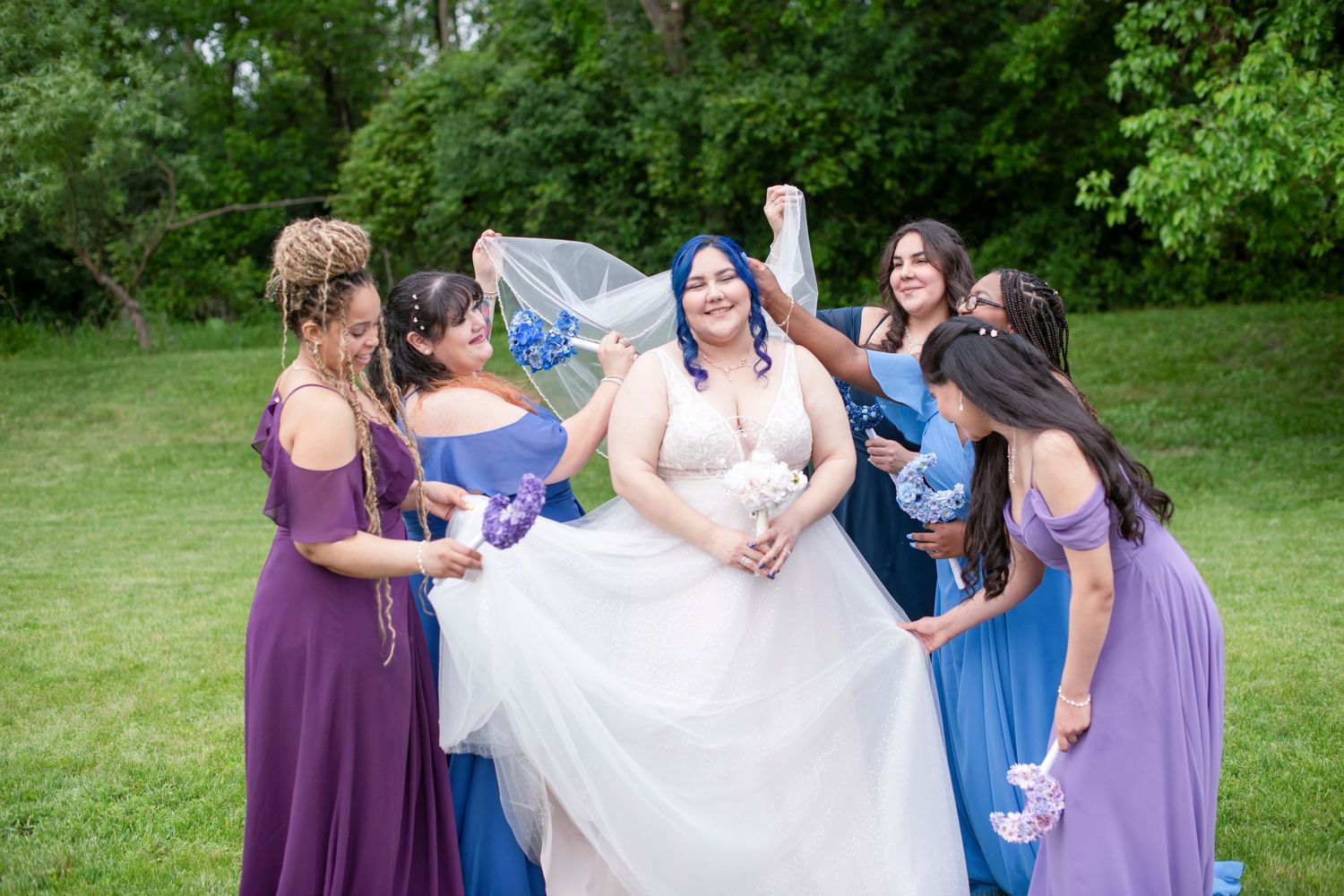 A group in purple and blue dresses gather outdoors for a joyful celebration on a sunny day.