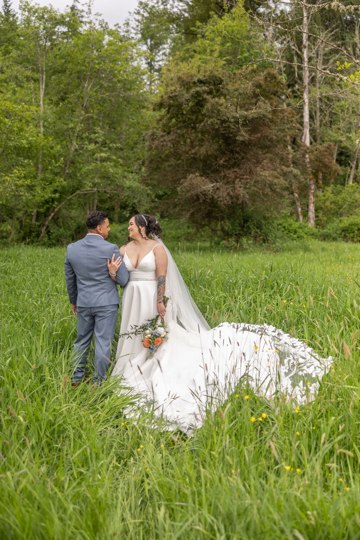 A couple in wedding attire sits together in a lush green meadow during a romantic outdoor photo session.