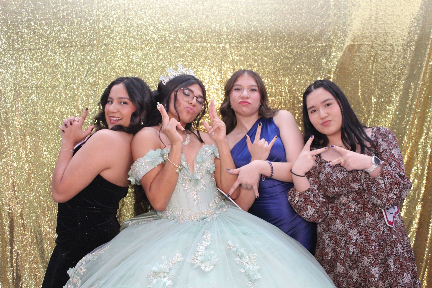 Group of people posing and having fun in front of a sparkly gold backdrop at a party or celebration event.