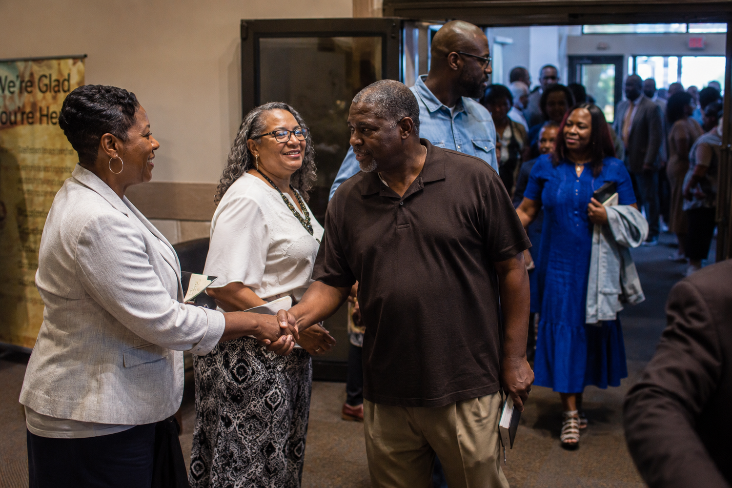 People greeting and shaking hands at a community gathering event in a church or community center.