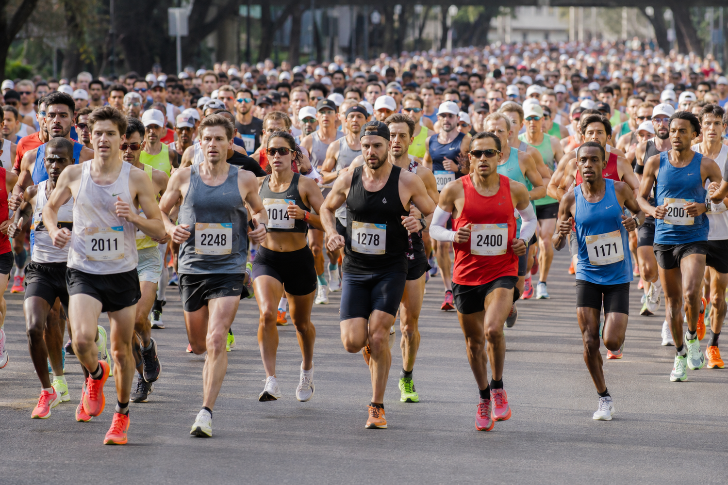 Large group of runners wearing race bibs competing in a city marathon on a sunny day.
