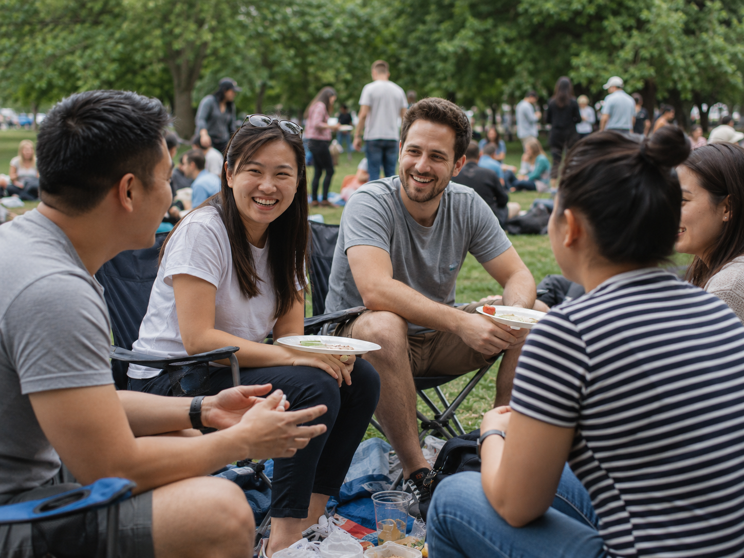 Friends laughing and socializing at an outdoor park gathering on a sunny day.