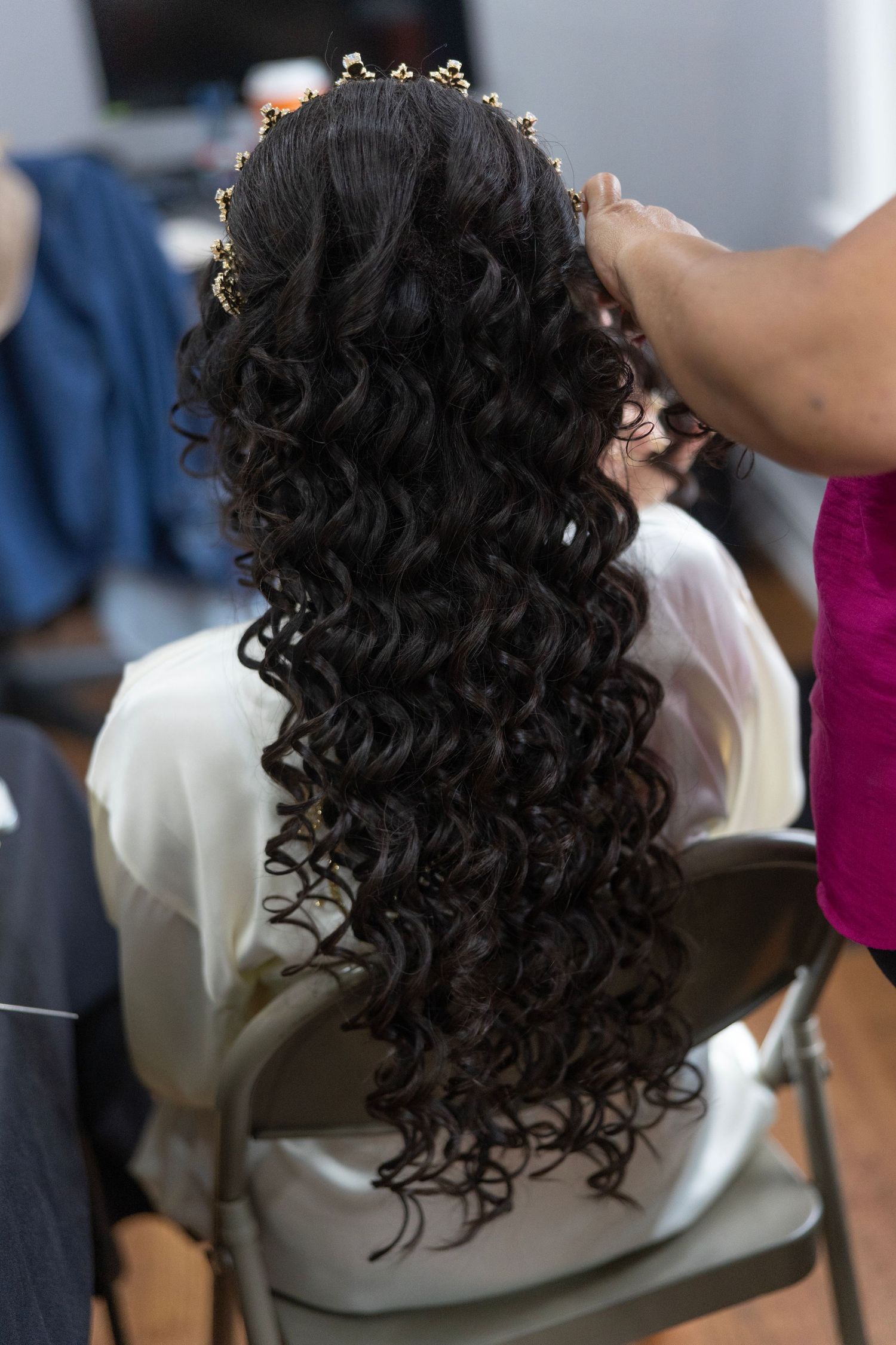 Back view of long dark curly hair adorned with gold pins, styled by a hairdresser for a formal event.