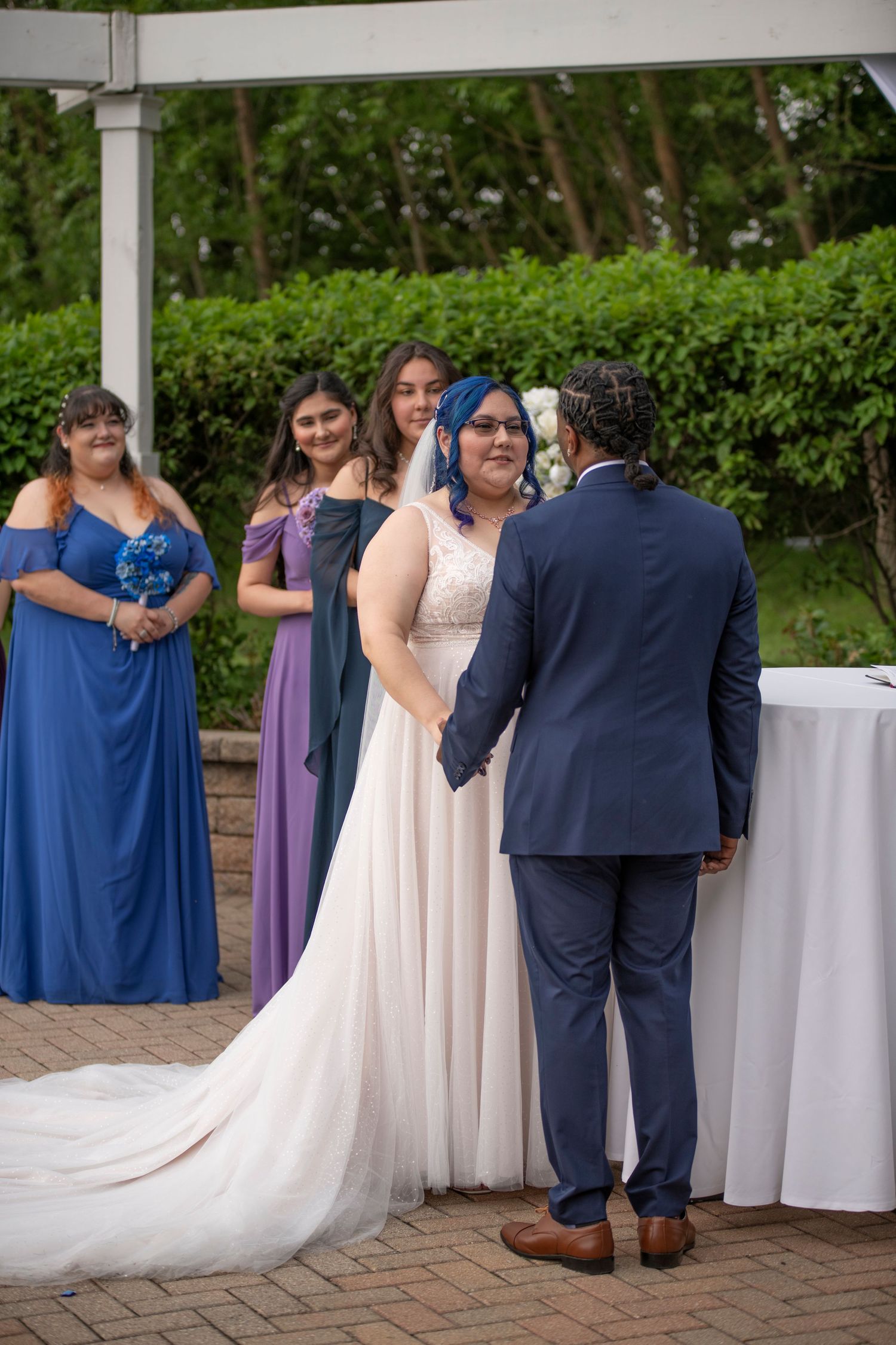 Wedding party members in navy blue and blush pink attire embrace during an outdoor reception on a brick patio.