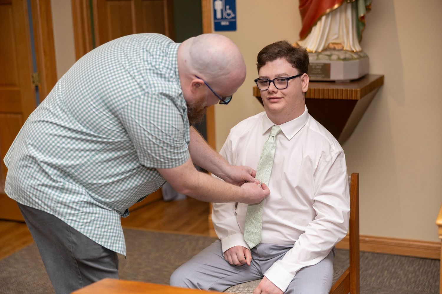 A series of four photos showing someone helping another person put on a tie in a formal setting.