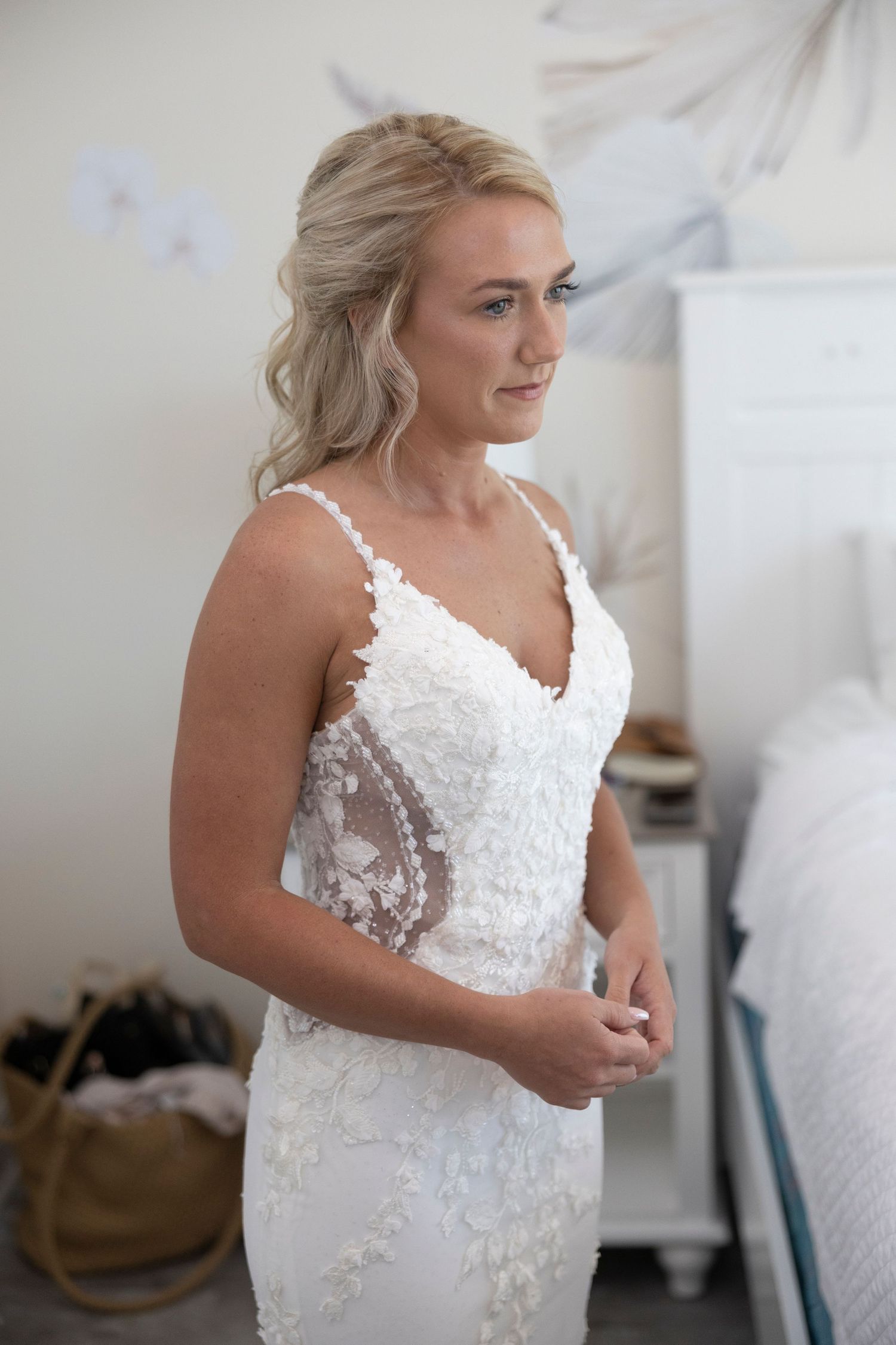 A bride in a white lace wedding dress with floral appliques poses in a bright room during her getting ready moments.