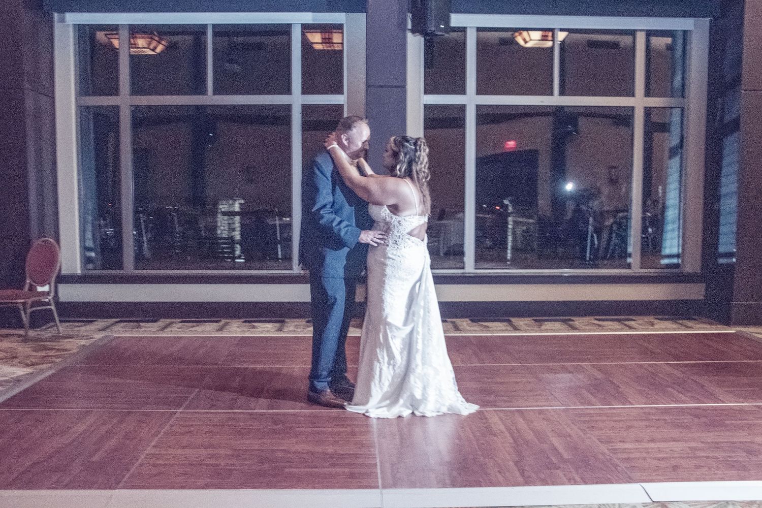 A couple shares their first dance as newlyweds on a wooden dance floor at their wedding reception.