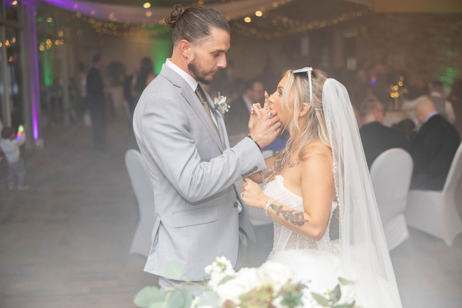 Two newlyweds share an intimate moment during their first dance at a reception with soft lighting and decorative elements.