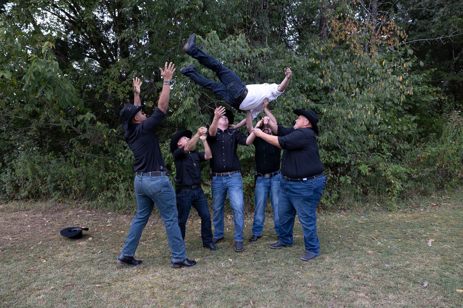 Groomsmen toss a friend in the air during outdoor wedding photo session.