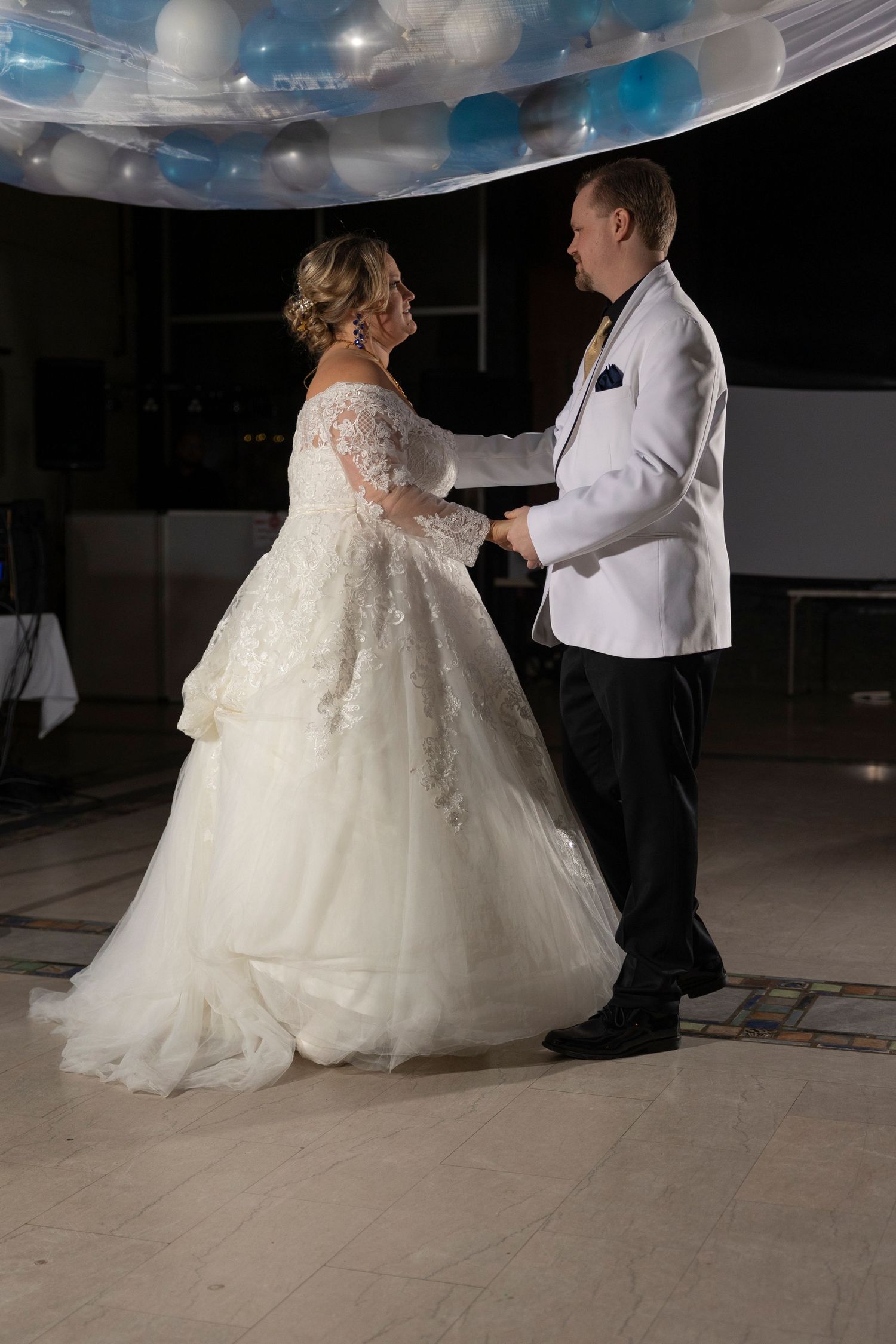 Bride and groom sharing their first dance at wedding reception under blue and white balloon ceiling decorations.