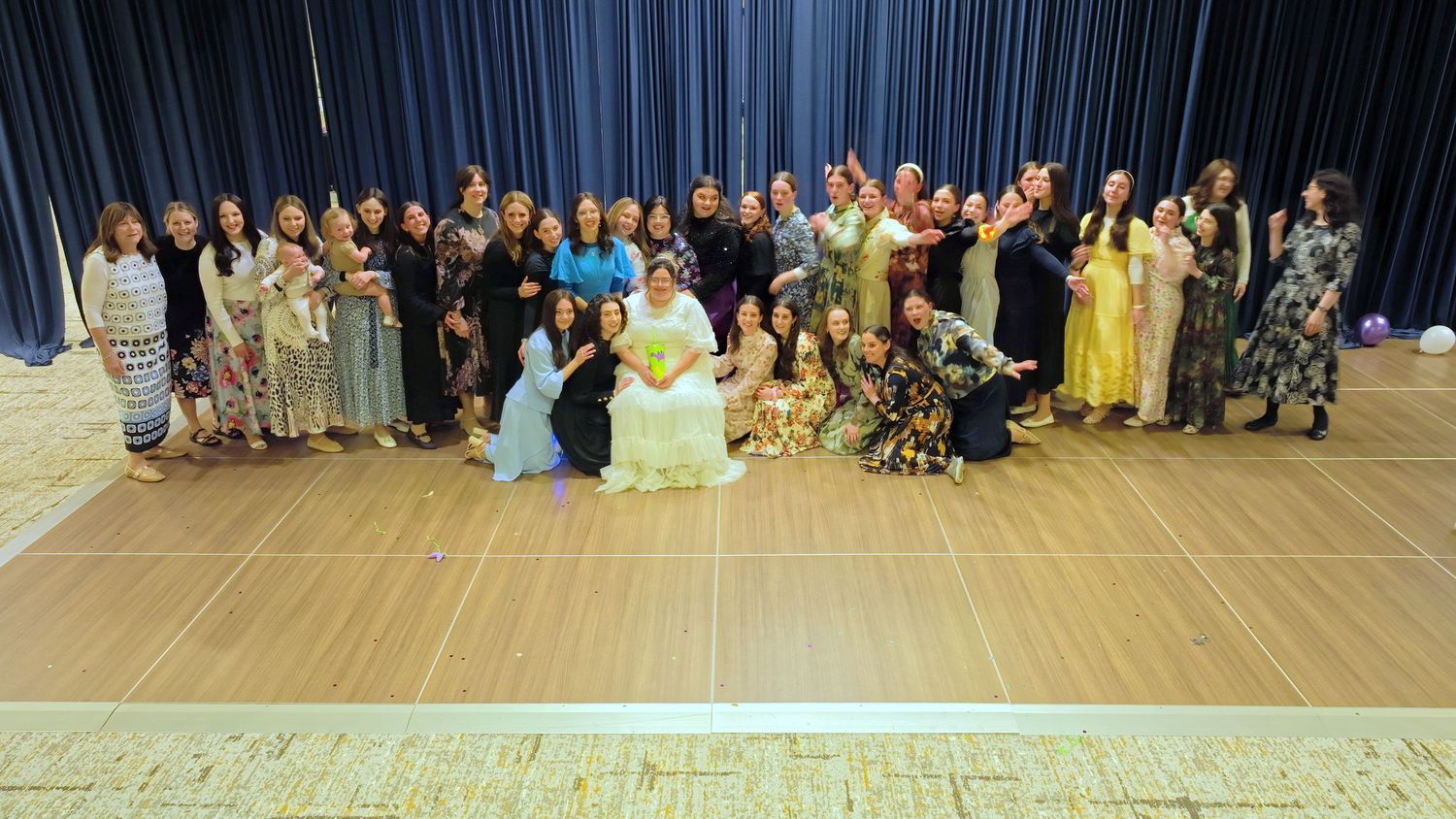 A large group of people posing together in formal attire at what appears to be a wedding or celebration event.