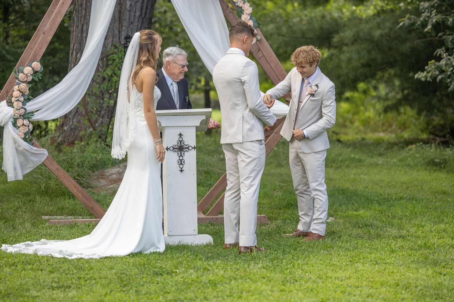 Wedding party in white attire poses together on a lush green lawn during an outdoor summer ceremony.