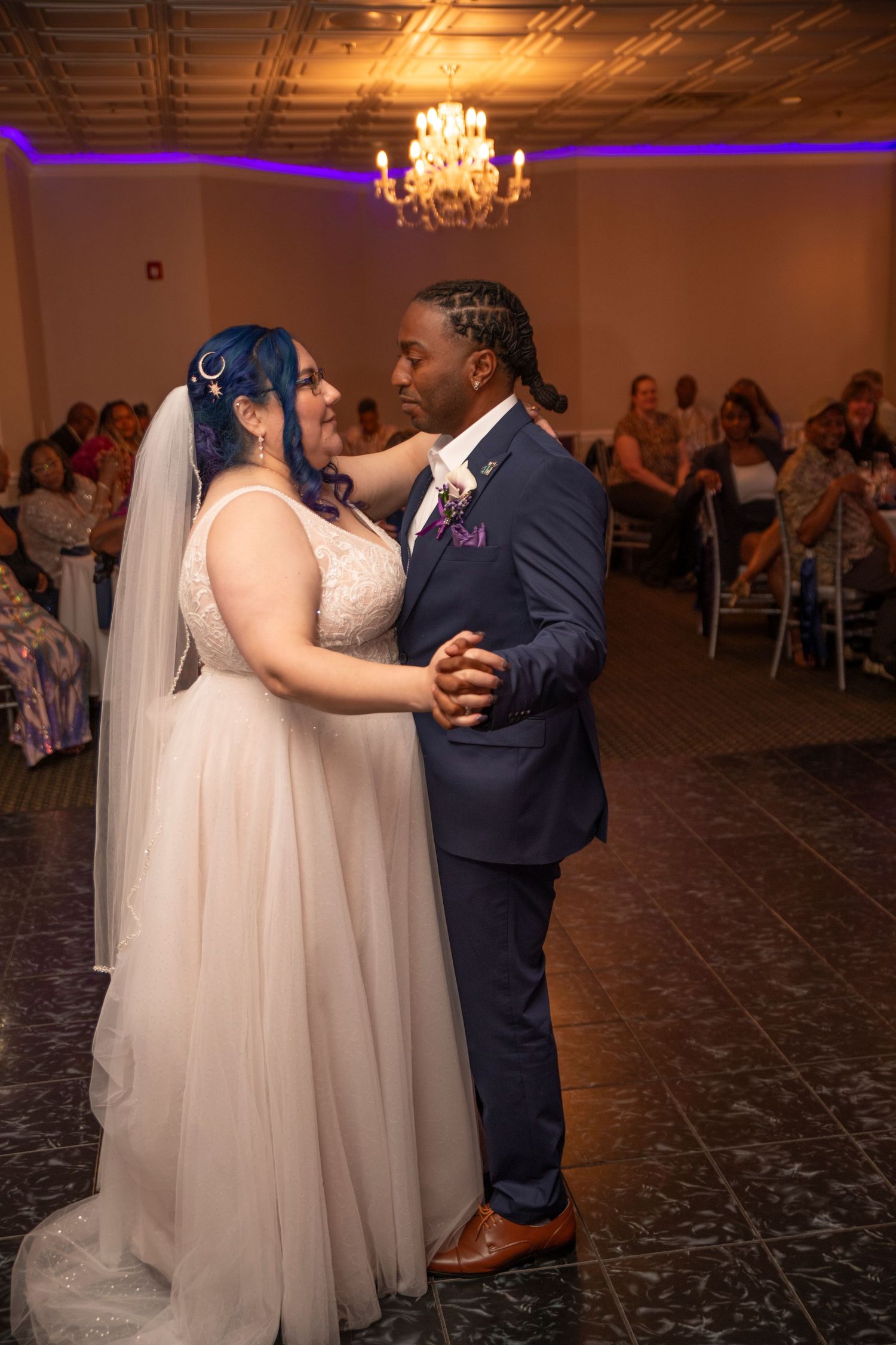 A couple shares a romantic first dance at their wedding reception under elegant crystal chandeliers.