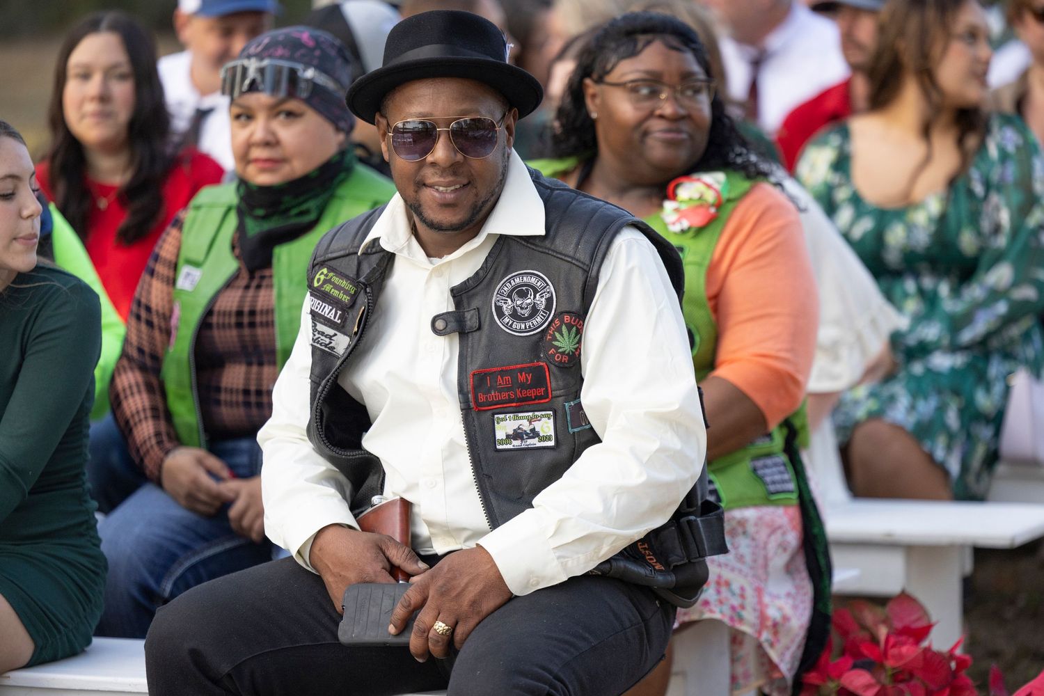 Diverse crowd of people watching and smiling at an outdoor event on a sunny day.