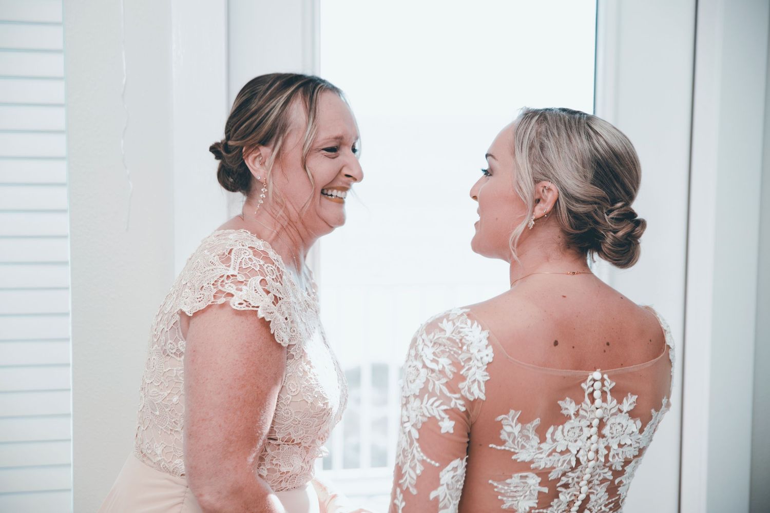 Two people in wedding attire share a joyful moment together while wearing elegant white dresses.