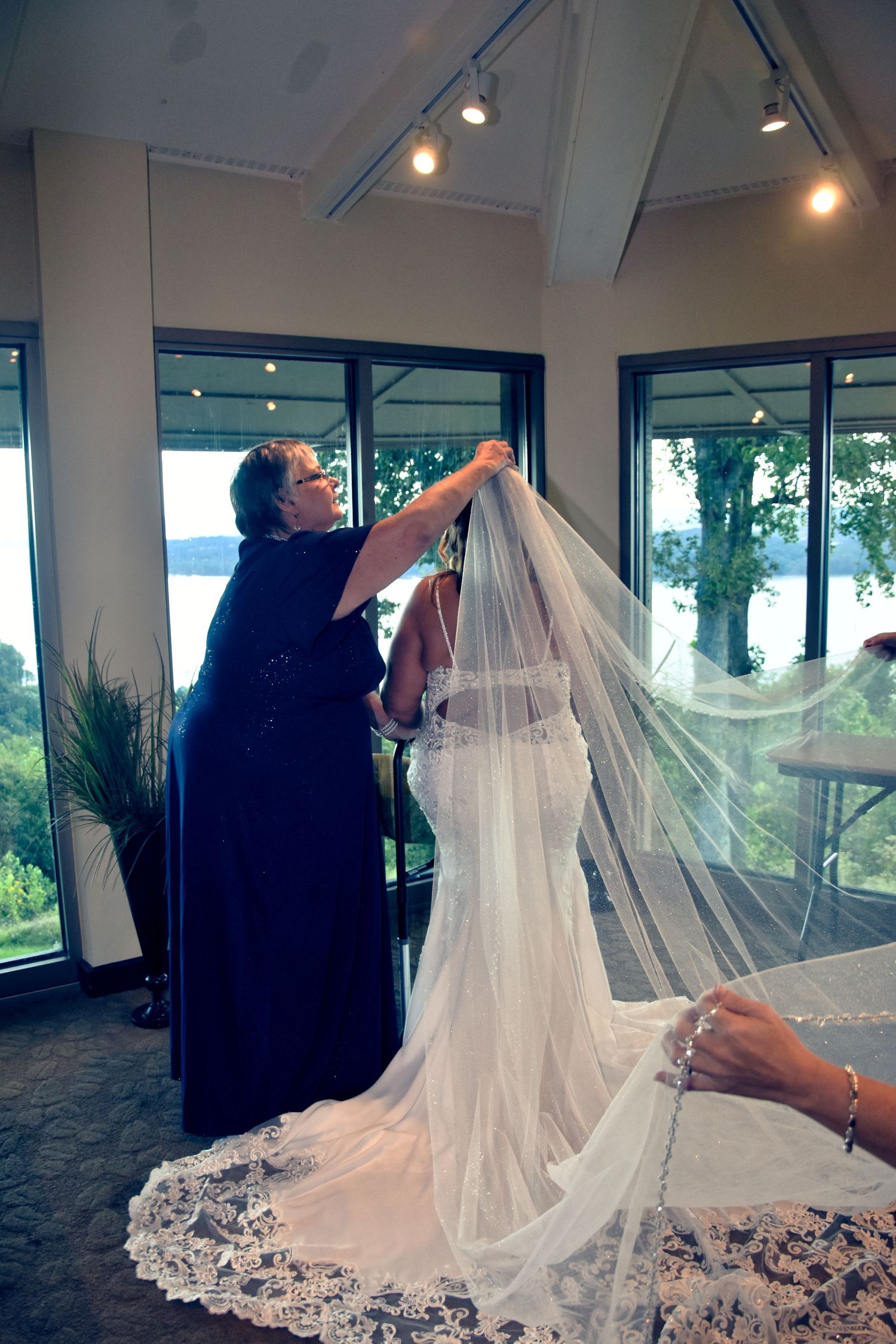 A wedding veil being adjusted and arranged in a bright room with large windows overlooking a scenic outdoor view.