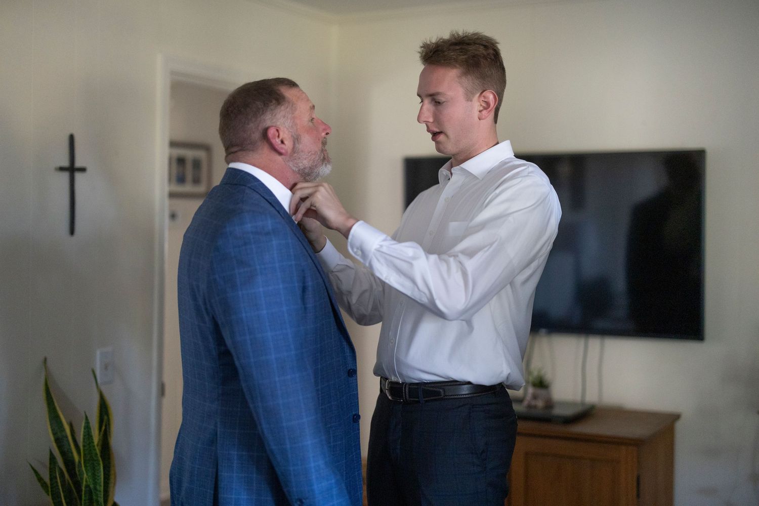 Two people in formal attire adjusting clothing and preparing for a formal event in an indoor setting.