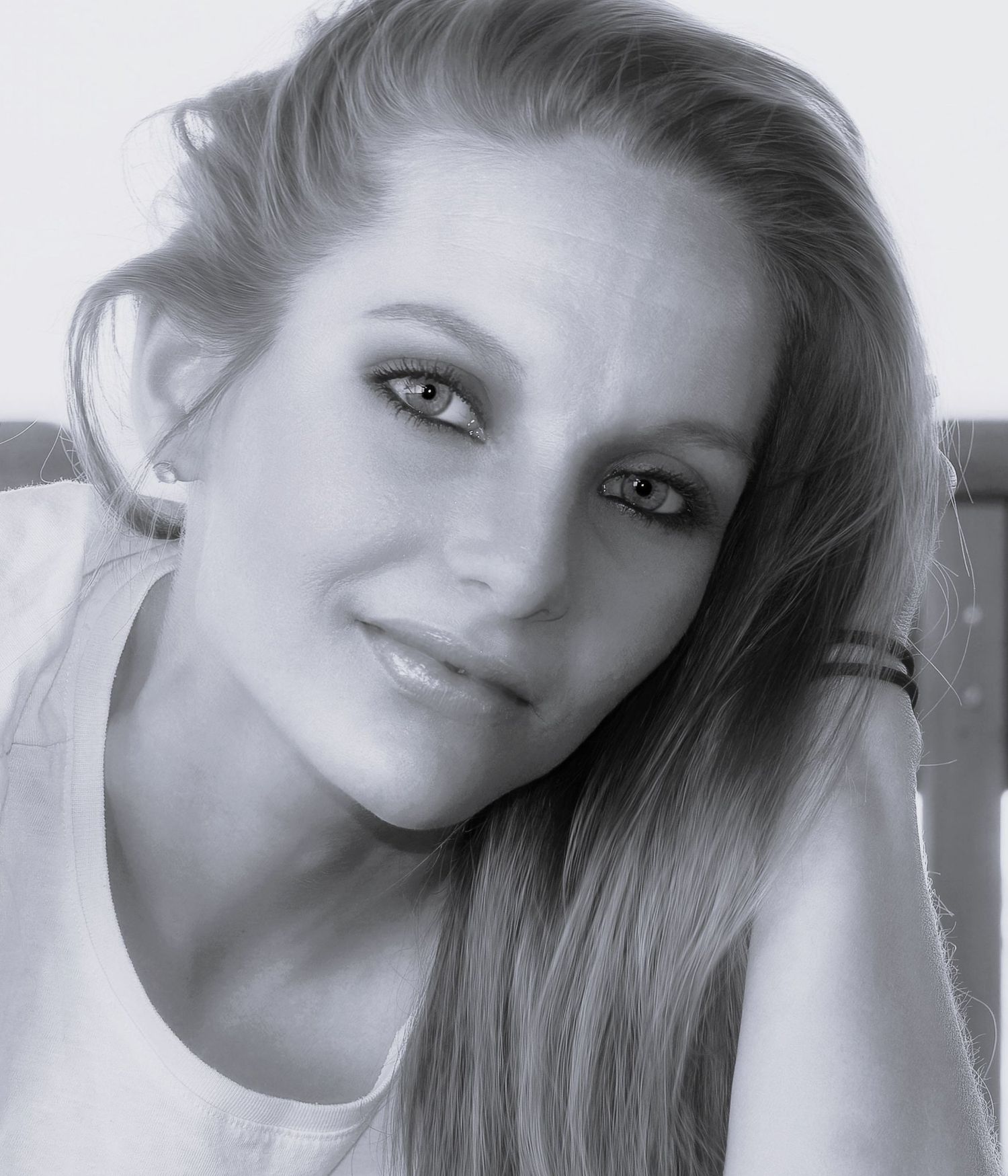 Black and white portrait of a young blonde woman smiling softly with natural makeup and long hair.