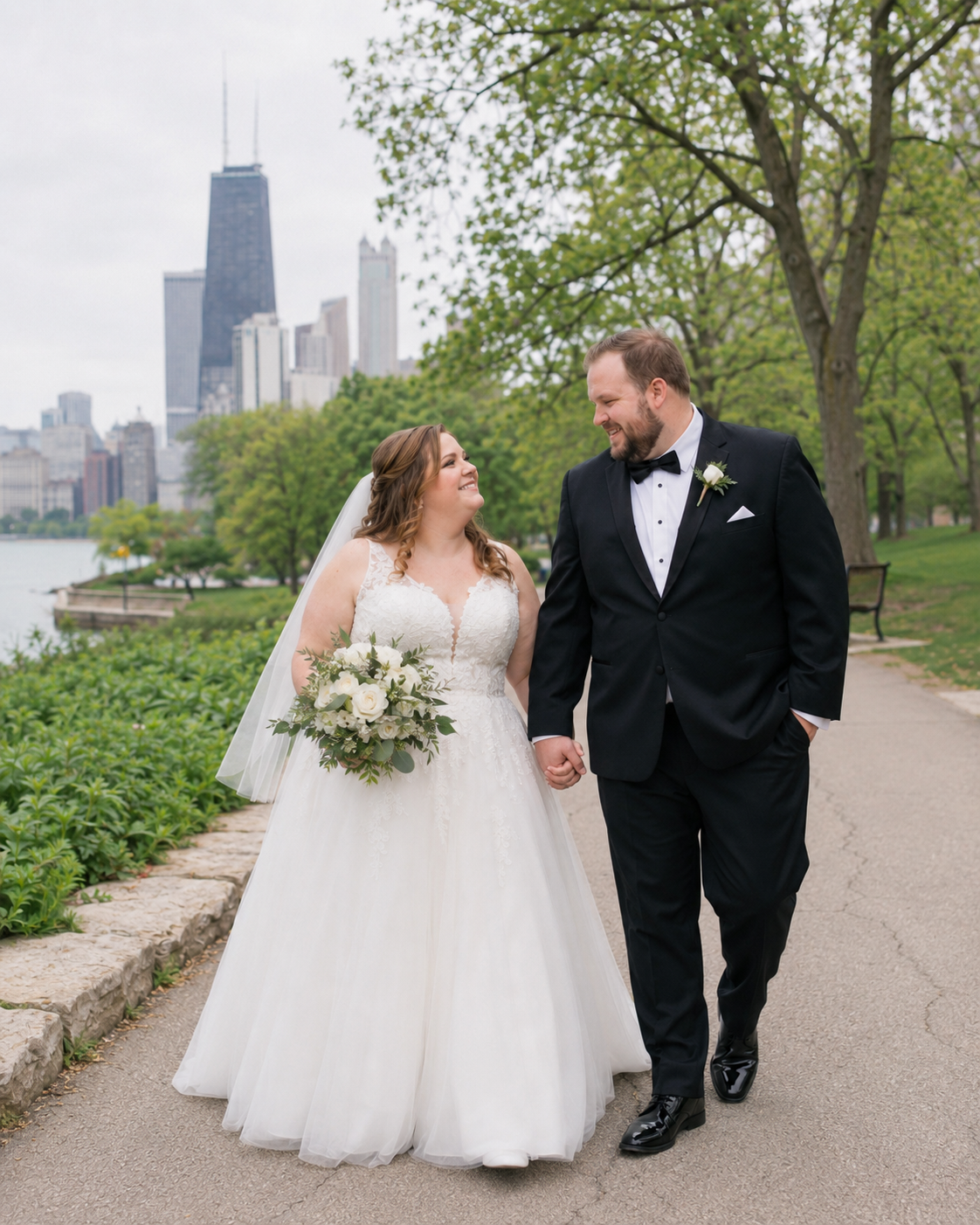 Bride and groom walk hand-in-hand on a lakeside path with the Chicago skyline in the background.