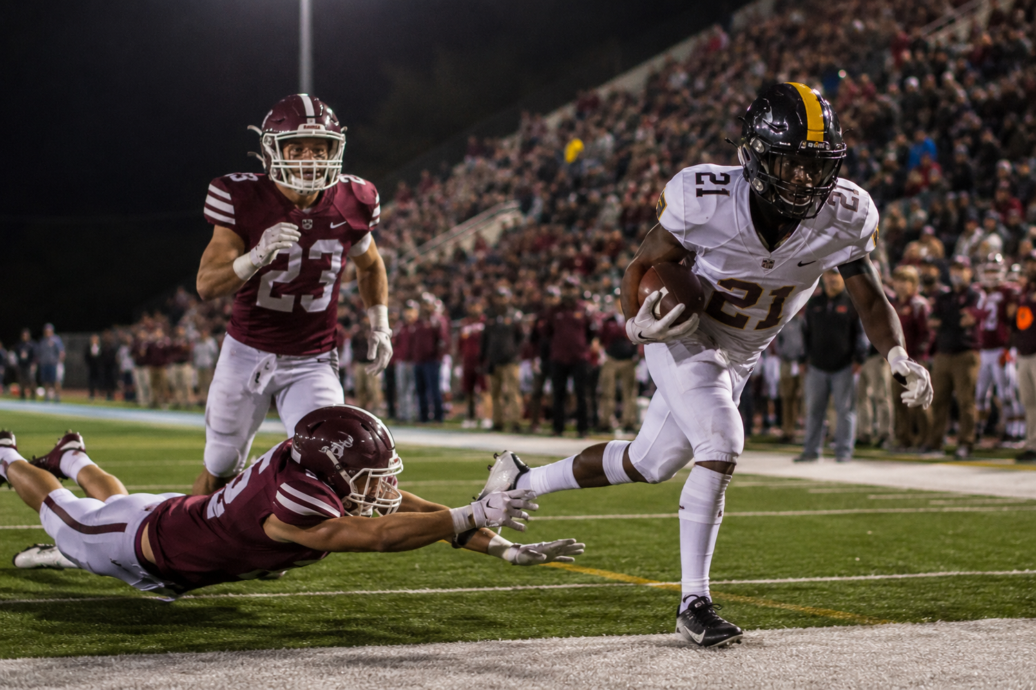 Football player in yellow jersey evades tackle near end zone during night game.