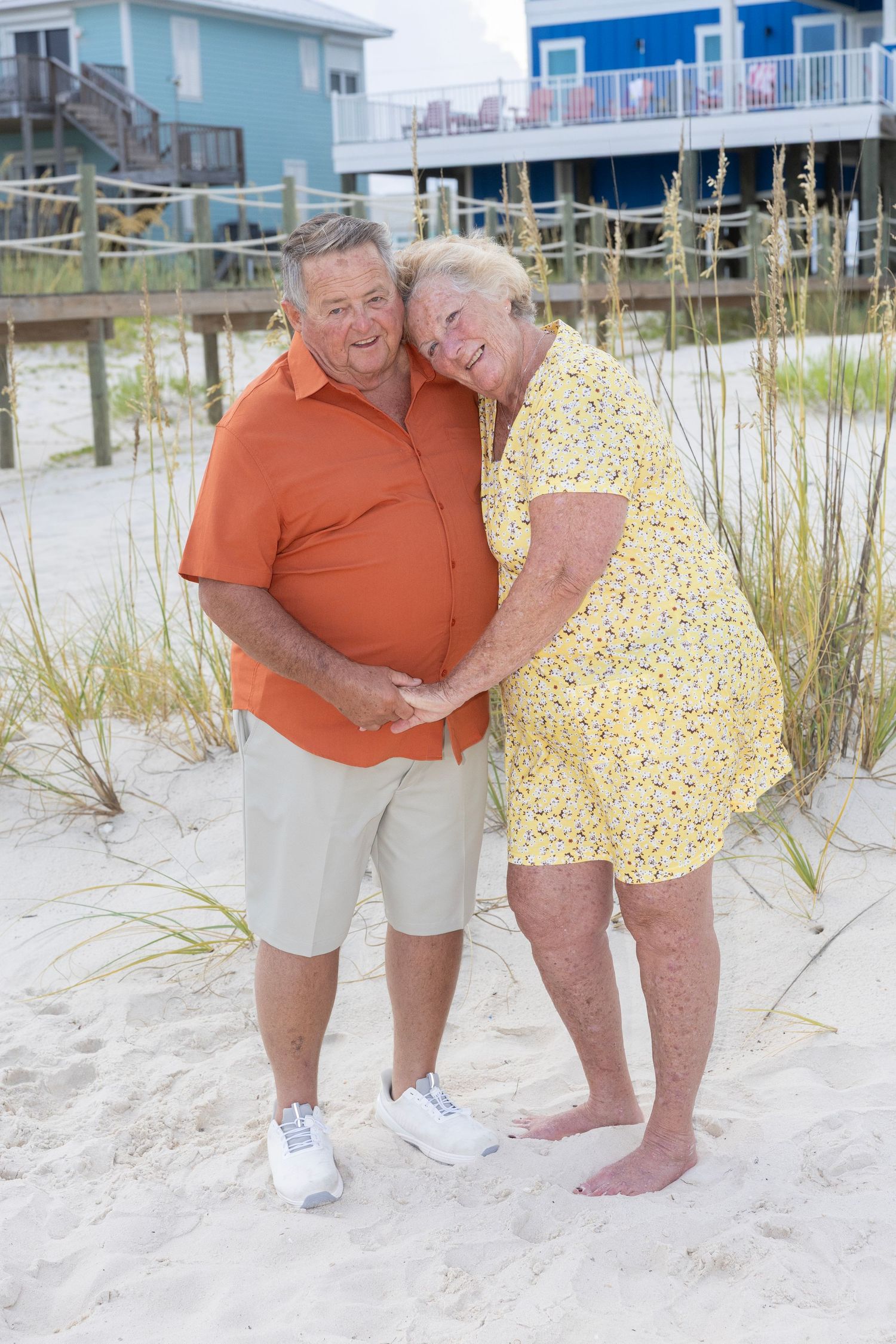 Happy couple enjoying a romantic moment together on a sunny beach with coastal homes in the background.