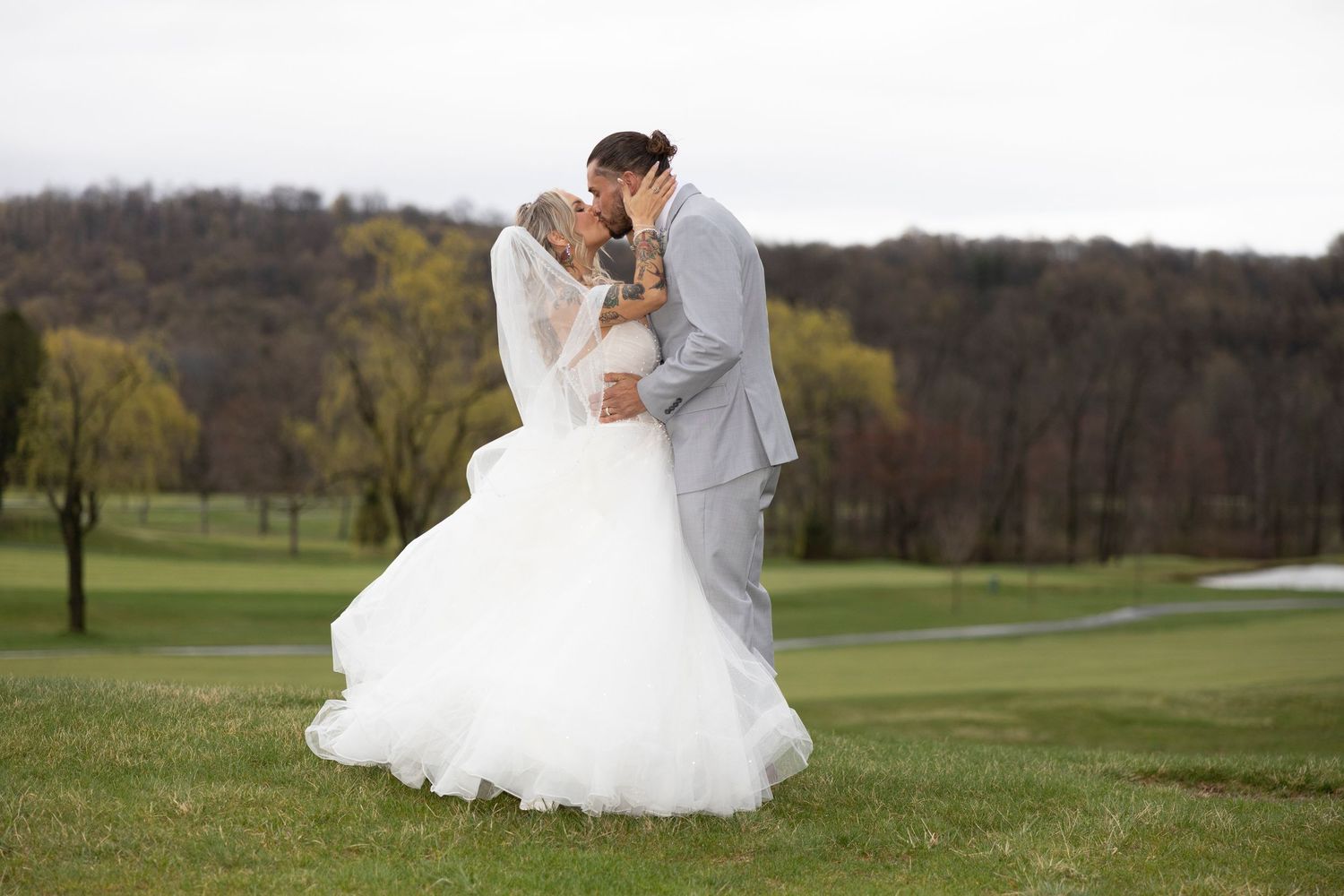 A couple shares a romantic moment together on a golf course during their wedding day, surrounded by rolling green hills.
