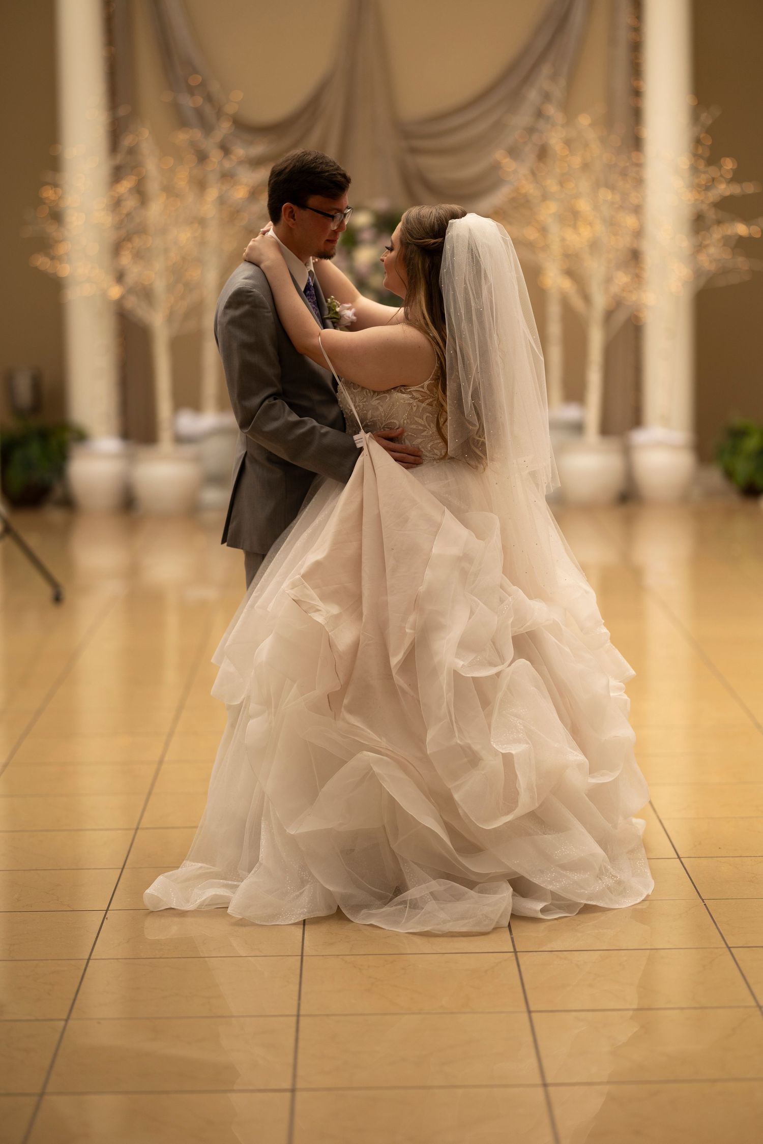A couple dances together in an elegant ballroom with their wedding attire flowing gracefully.