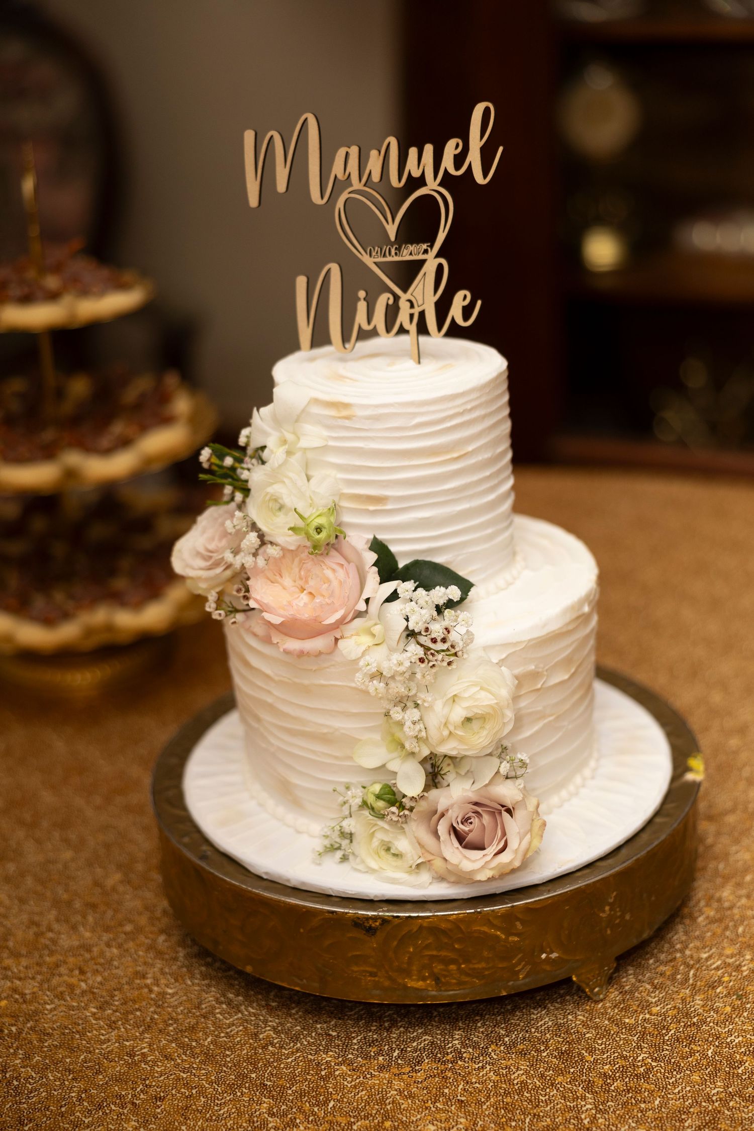 White wedding cake with textured buttercream frosting decorated with pink roses and baby's breath on a gold charger plate.