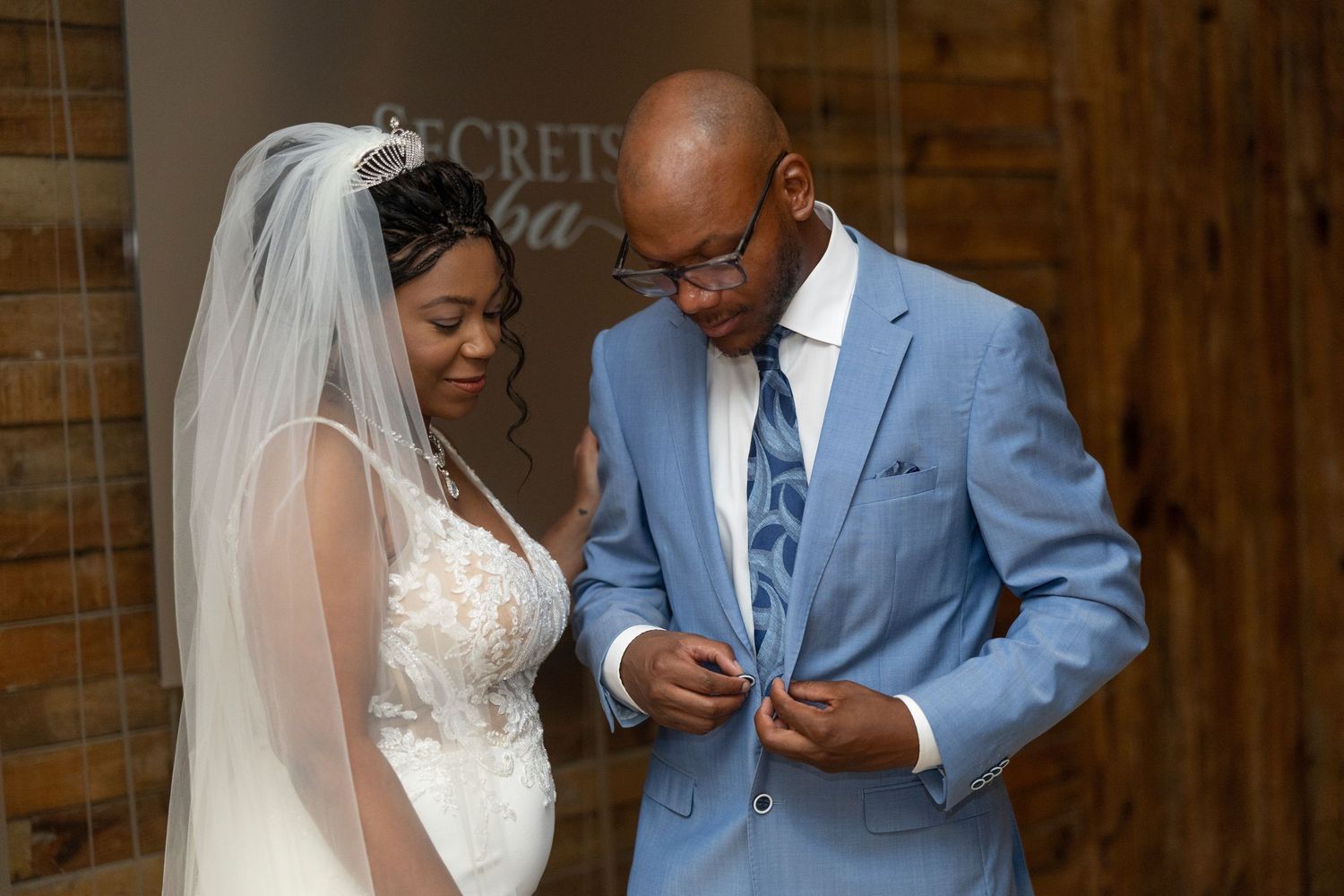 A couple shares a tender moment on their wedding day, with the bride in white lace and groom in light blue suit.