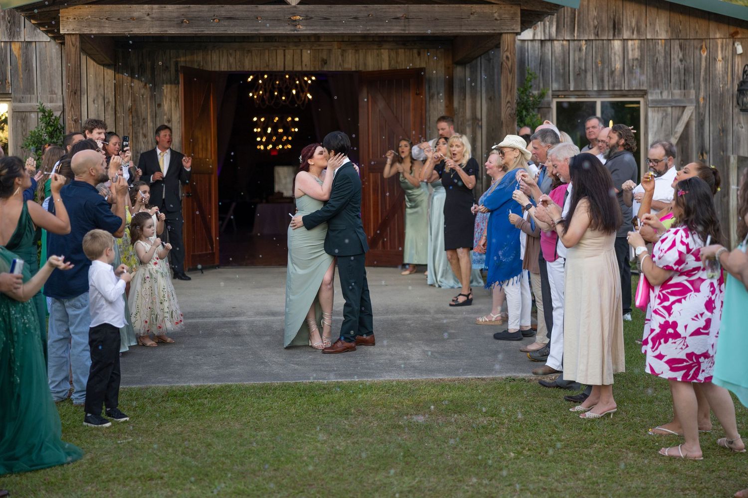 Wedding guests dance and socialize outdoors at a rustic barn venue during an evening celebration.
