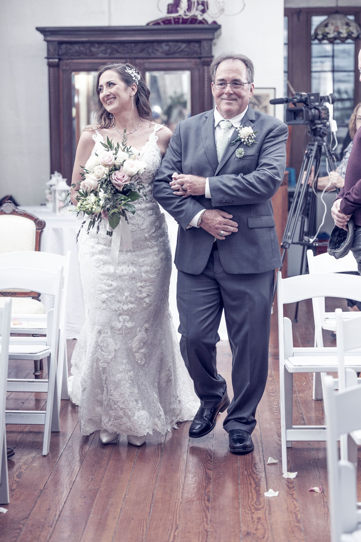 Wedding couple shares a playful dance move on a wooden floor surrounded by white chairs during their reception celebration.