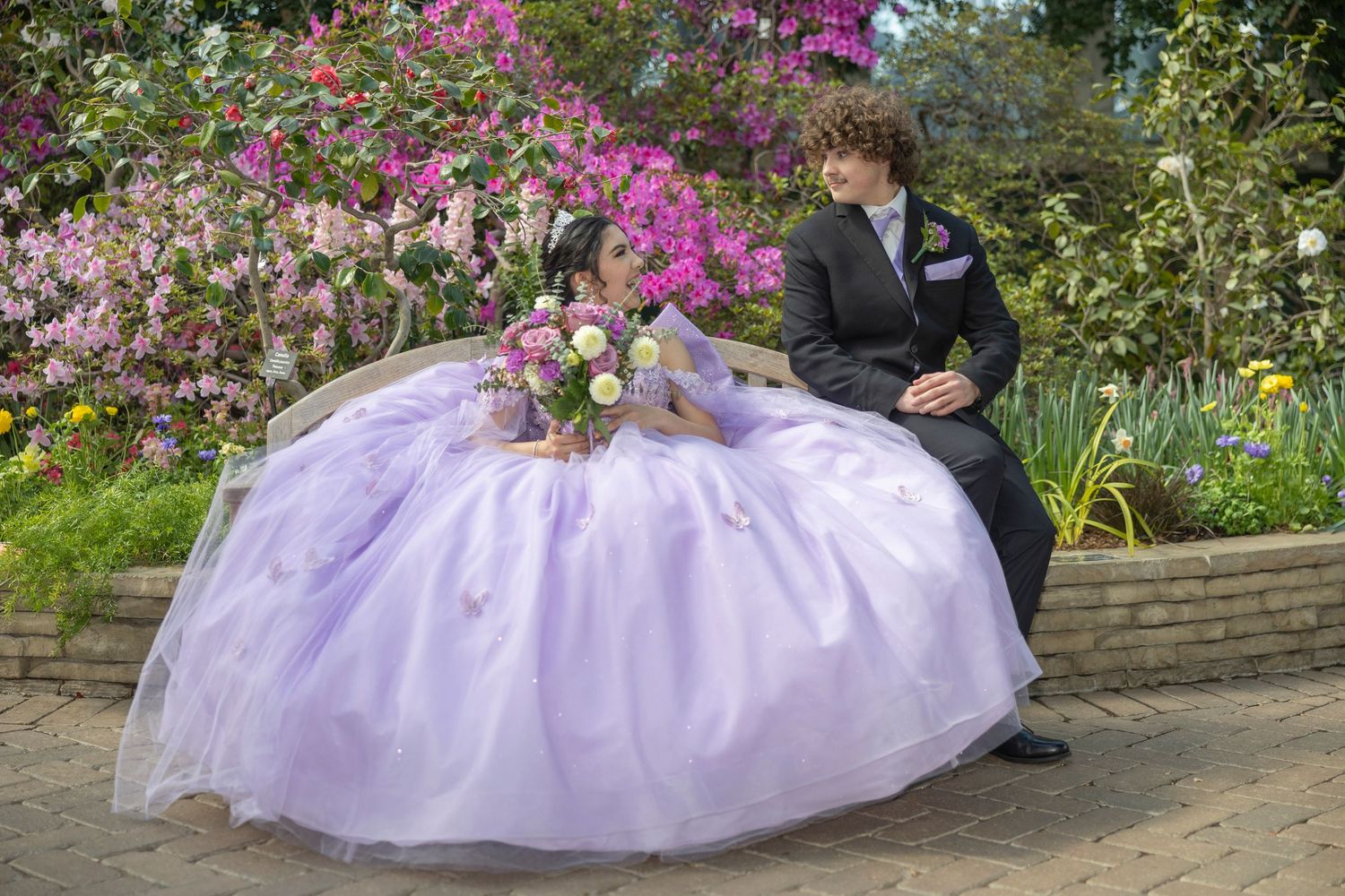 A lavender tulle wedding dress billows gracefully in a garden setting surrounded by vibrant pink flowers and greenery.