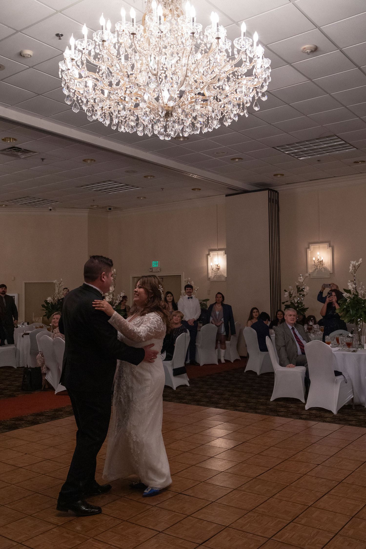 A couple performs a romantic dance under an elegant crystal chandelier during a wedding reception.