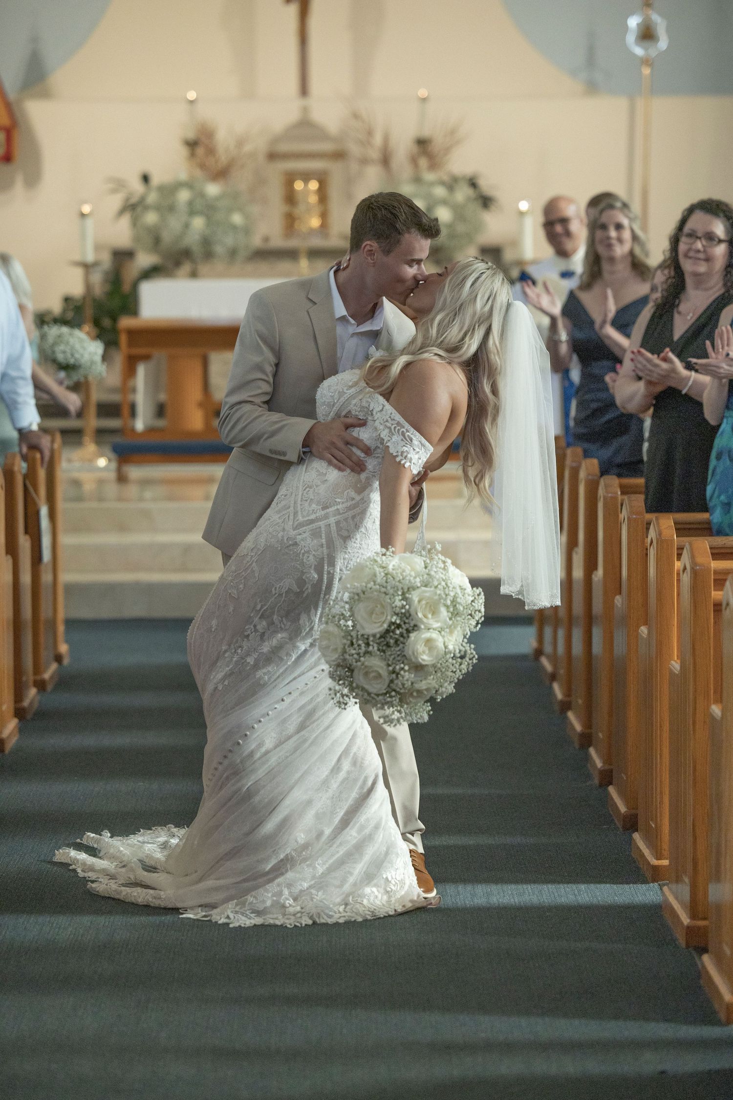 A romantic wedding couple dips during their first dance in a church aisle with green carpet and wooden pews.