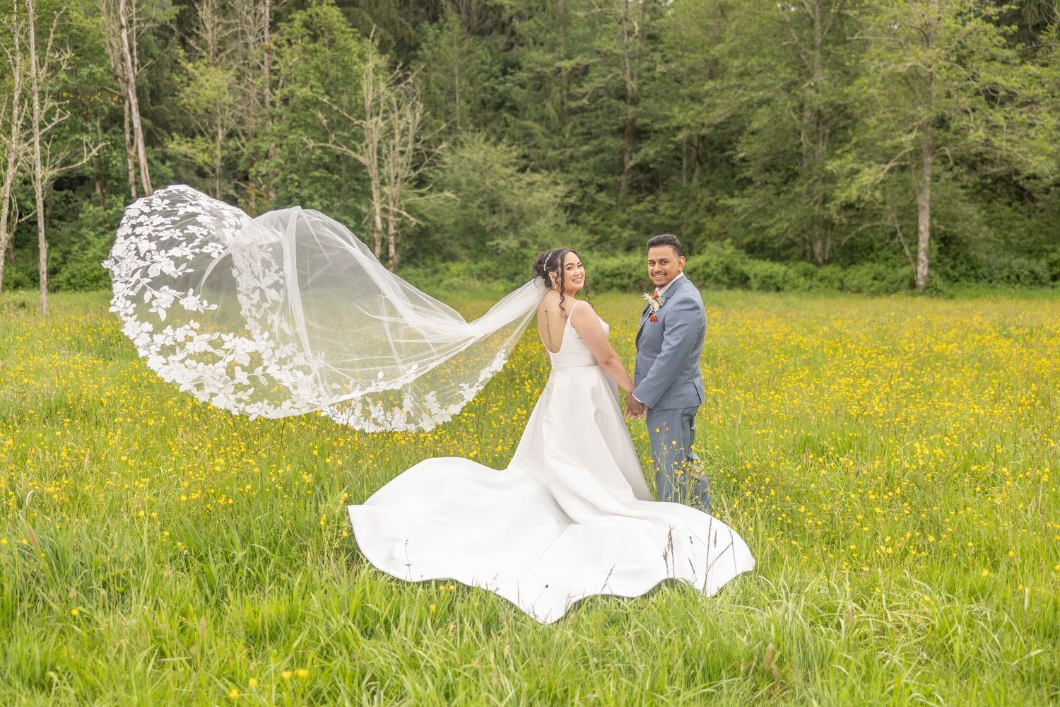 A white wedding veil flows gracefully in the wind across a vibrant yellow wildflower meadow on a sunny day.