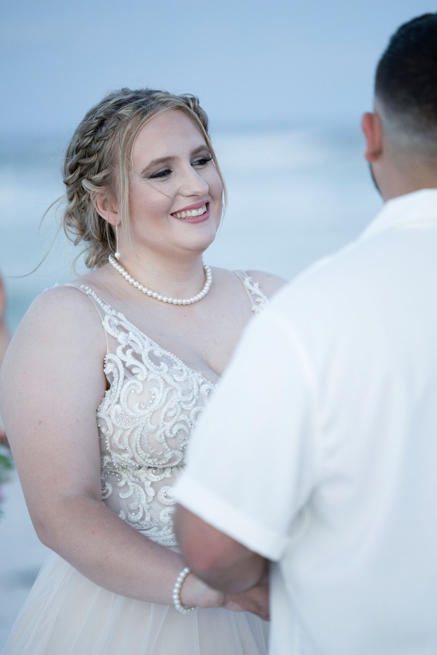 A bride in a white lace dress with pearl necklace shares candid moments during a wedding photoshoot outdoors.