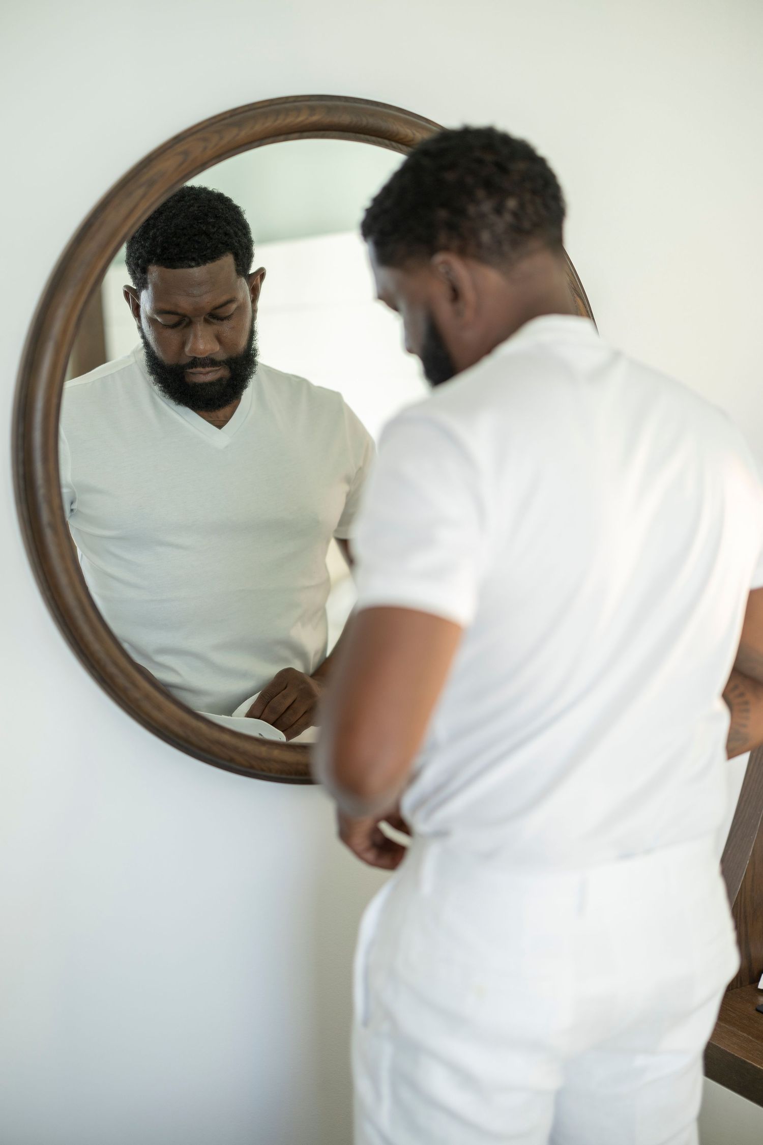 A sequence of mirror reflections shows two people in white shirts examining themselves in a round wooden framed mirror.