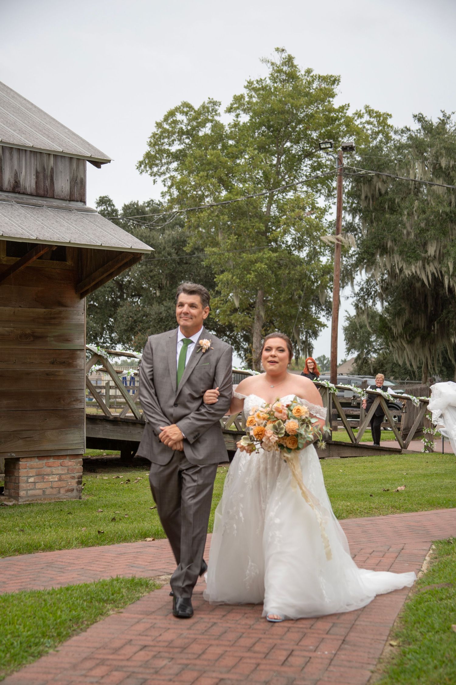 A couple in wedding attire sits together on brick steps outside a rustic wooden building surrounded by green trees.