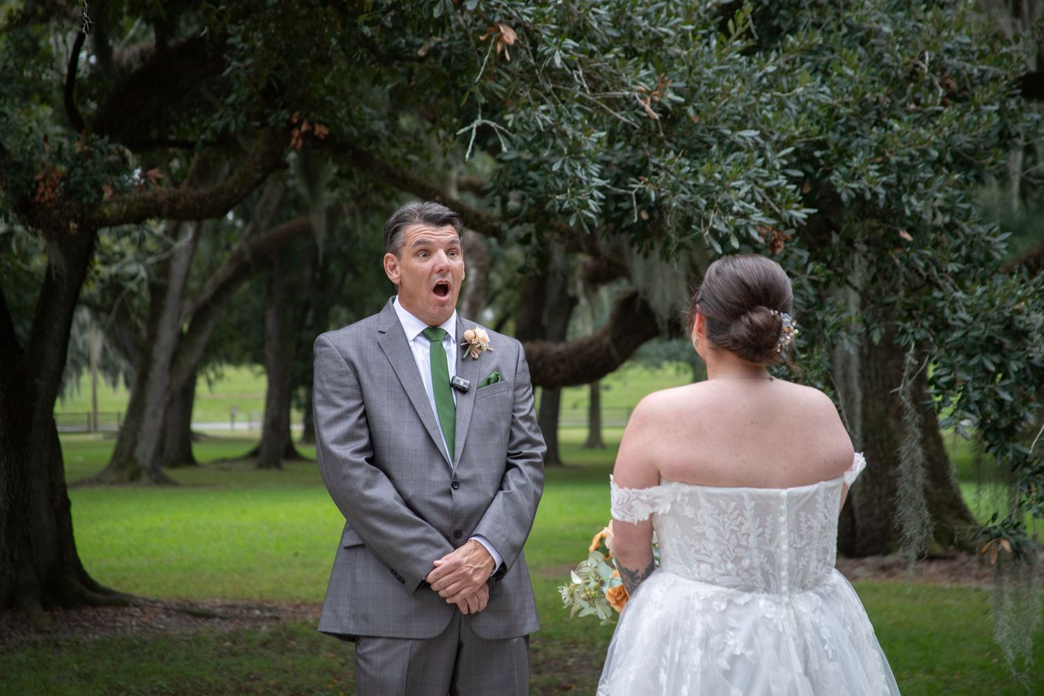 Wedding party poses under oak trees in a park wearing gray suits and white dresses.