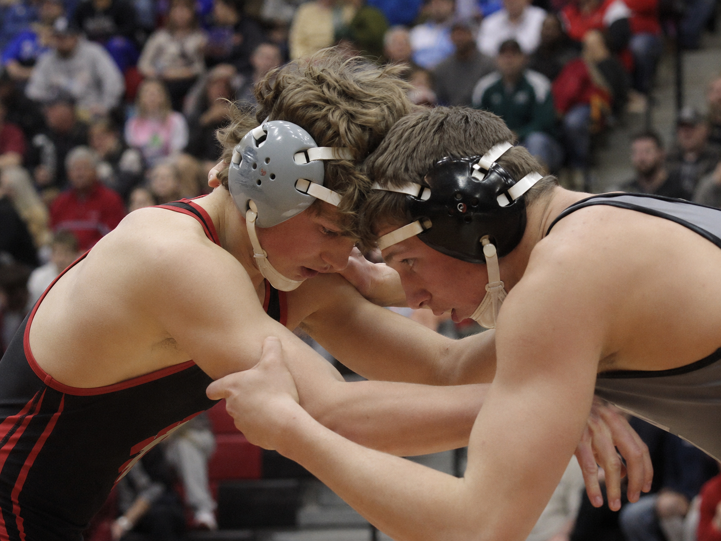 Two high school wrestlers in headgear grapple closely during an intense wrestling competition match.
