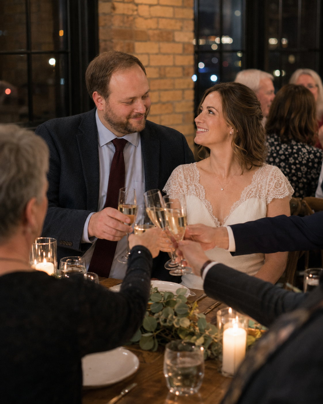 Bride and groom toasting champagne glasses with guests at elegant candlelit wedding reception dinner.