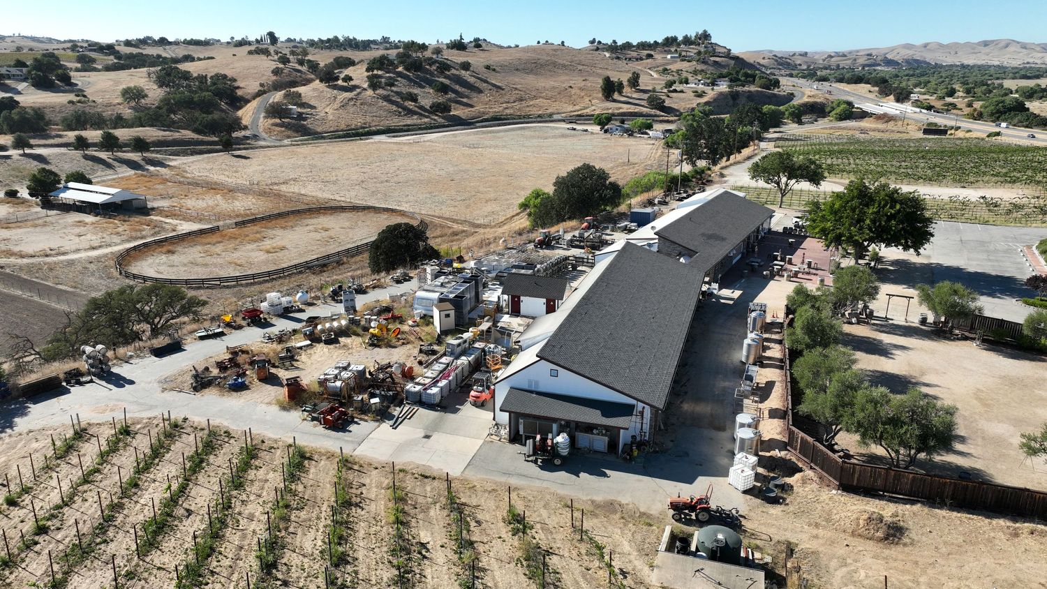 Aerial view of a rural California winery and equipment yard surrounded by vineyards and rolling hills.