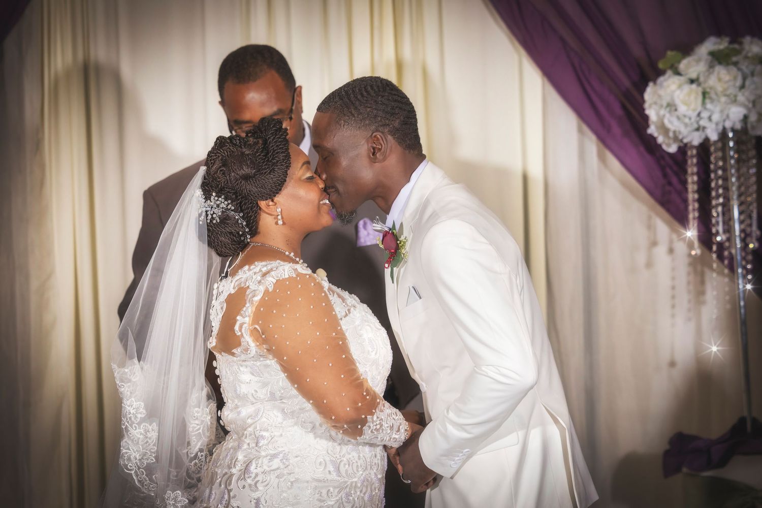 A bride and groom share their first kiss at the altar during a elegant wedding ceremony with purple drapes.